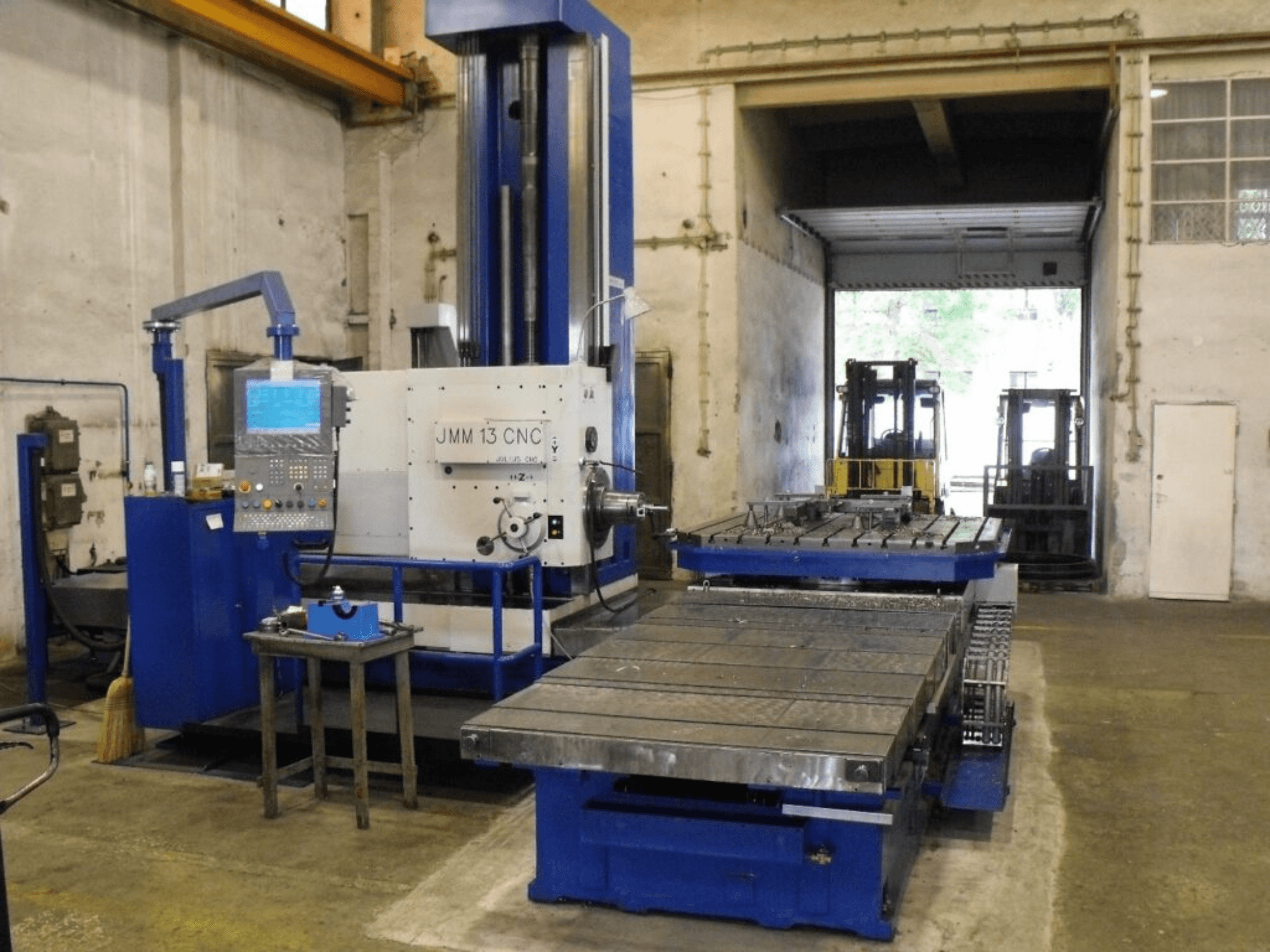 Фрезерний верстат з ЧПК JMM 13 в майстерні, вид спереду, з панеллю керування, великим робочим столом і промисловим фоном.