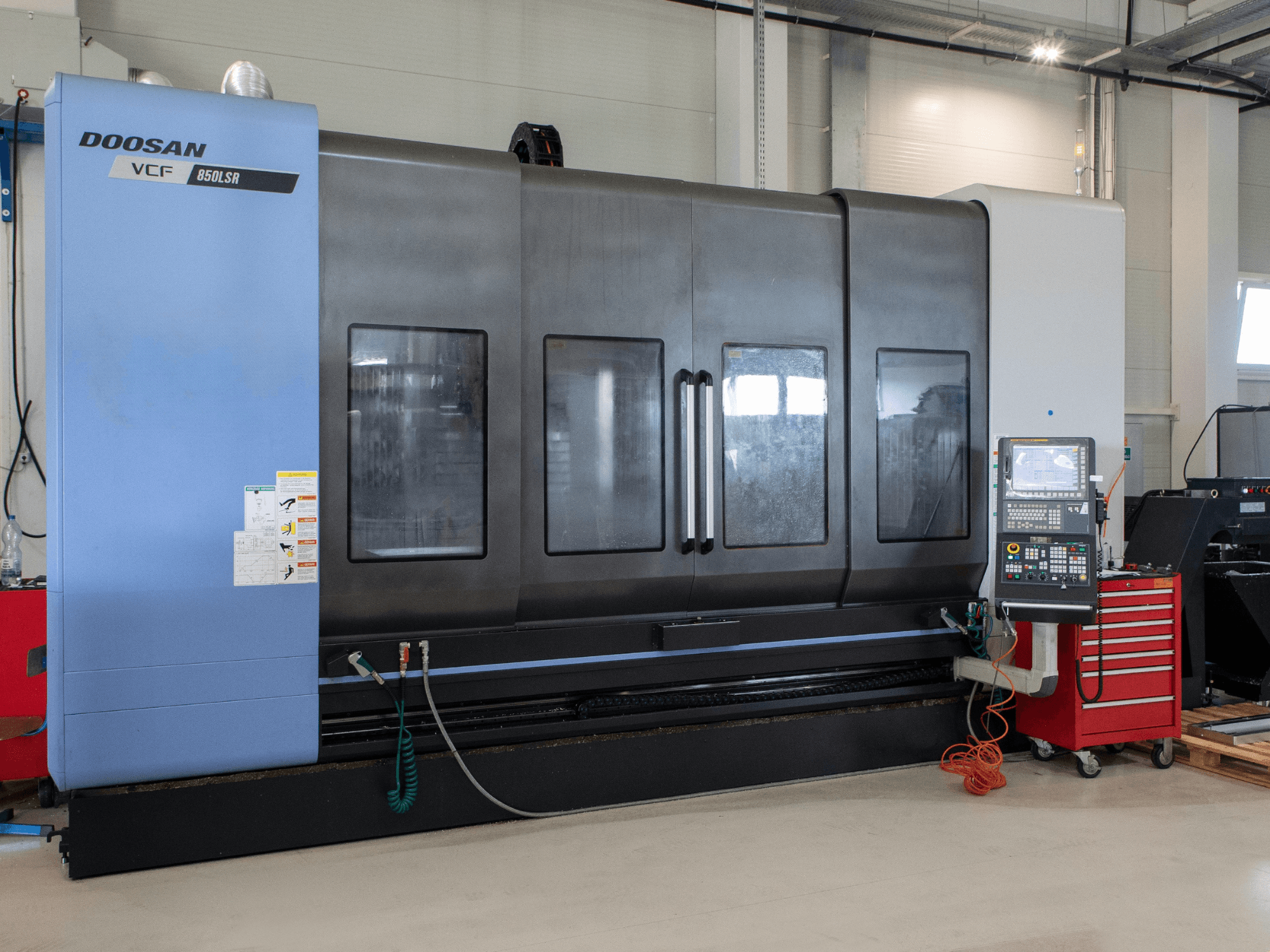 Токарно-фрезерний центр DOOSAN VCF850, вид спереду; оснащений великими подвійними вікнами, панеллю керування та відсіком для зберігання інструментів. Ідеально підходить для механічної обробки.