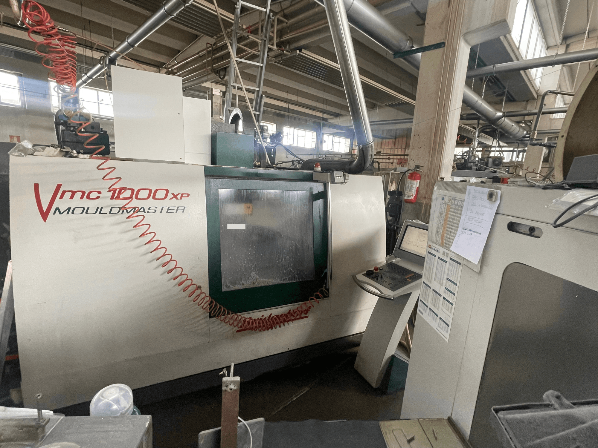 Вертикальний обробний центр Bridgeport VMC 1000, вид спереду, на якому видно панель управління та деталі верстата в промисловому середовищі.
