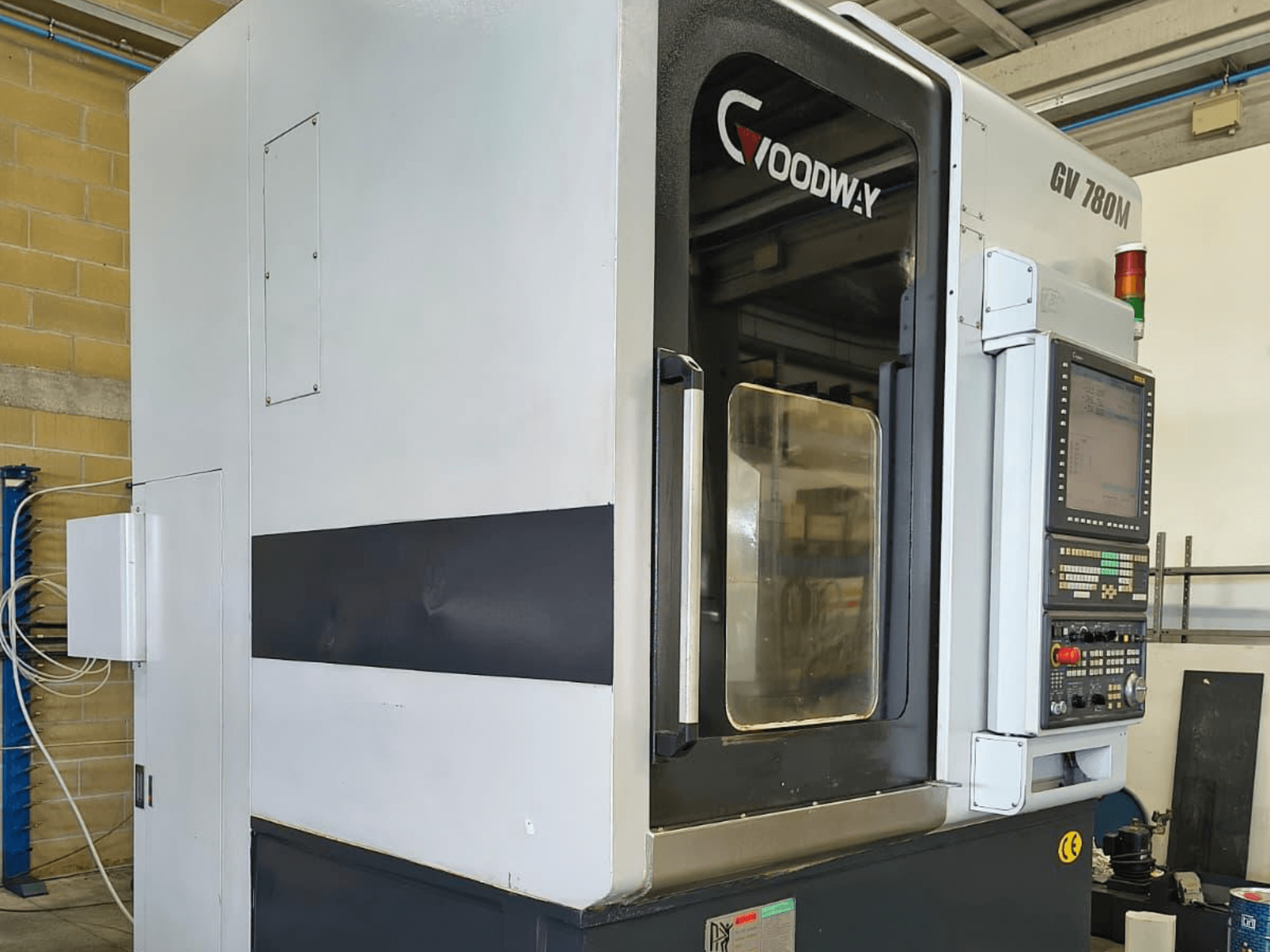 Вертикальний токарний верстат Goodway GV 780 M, вид збоку, демонструє панель управління, функції безпеки та чистий зовнішній дизайн.