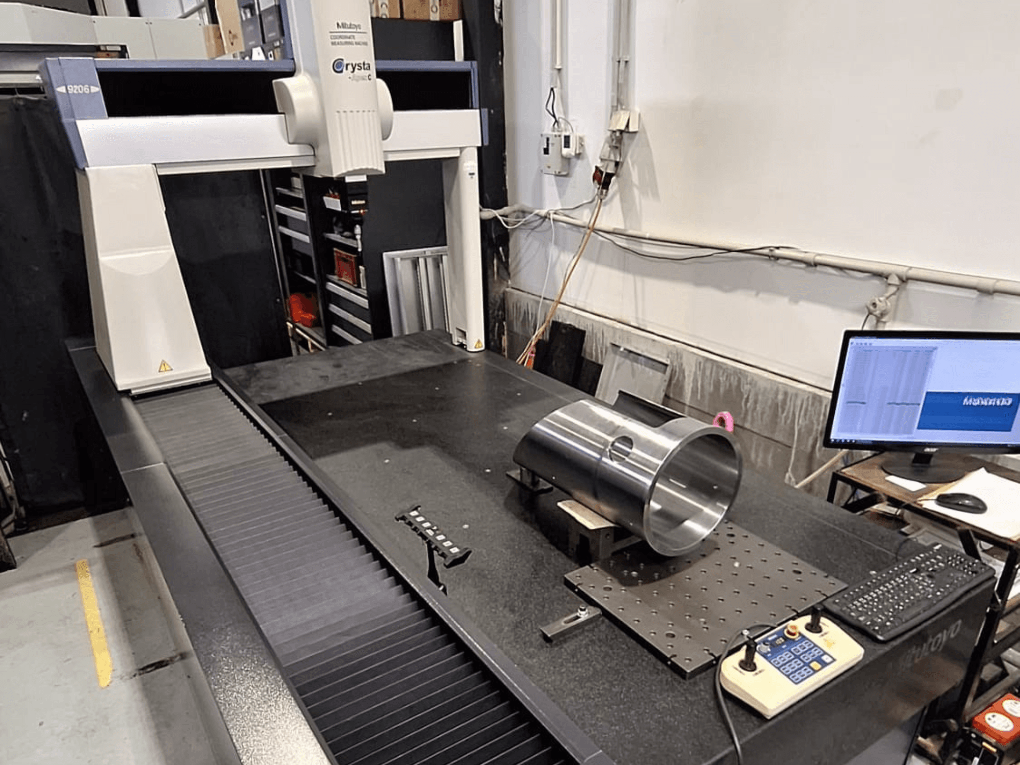 КВМ Mitutoyo Crysta-Apex C9206, вид спереду, вимірює циліндричну металеву деталь на чорній гранітній плиті.