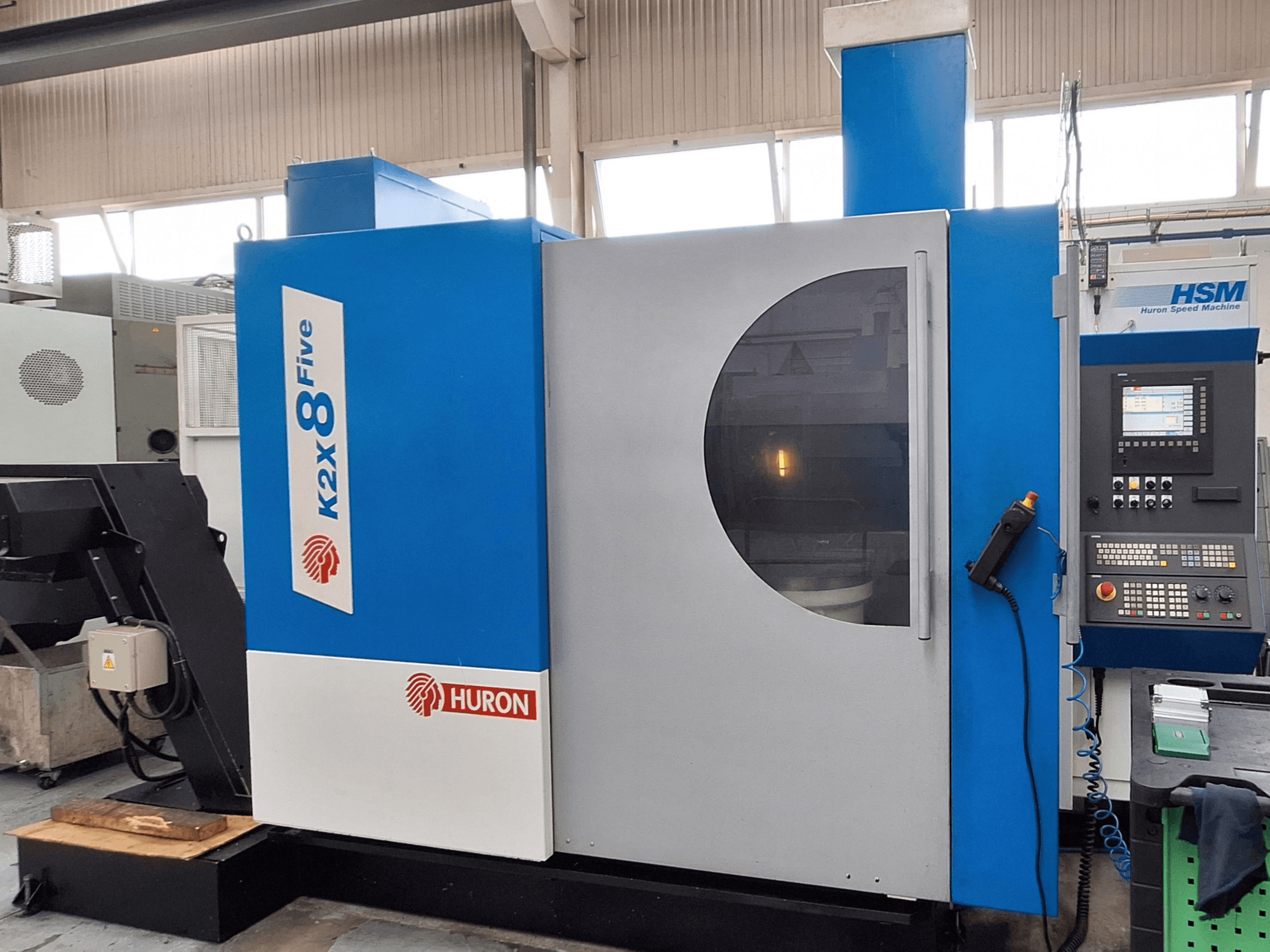 Портальний фрезерний верстат Huron K2X 8 Five, вид спереду, на якому видно панель управління та велике оглядове вікно.