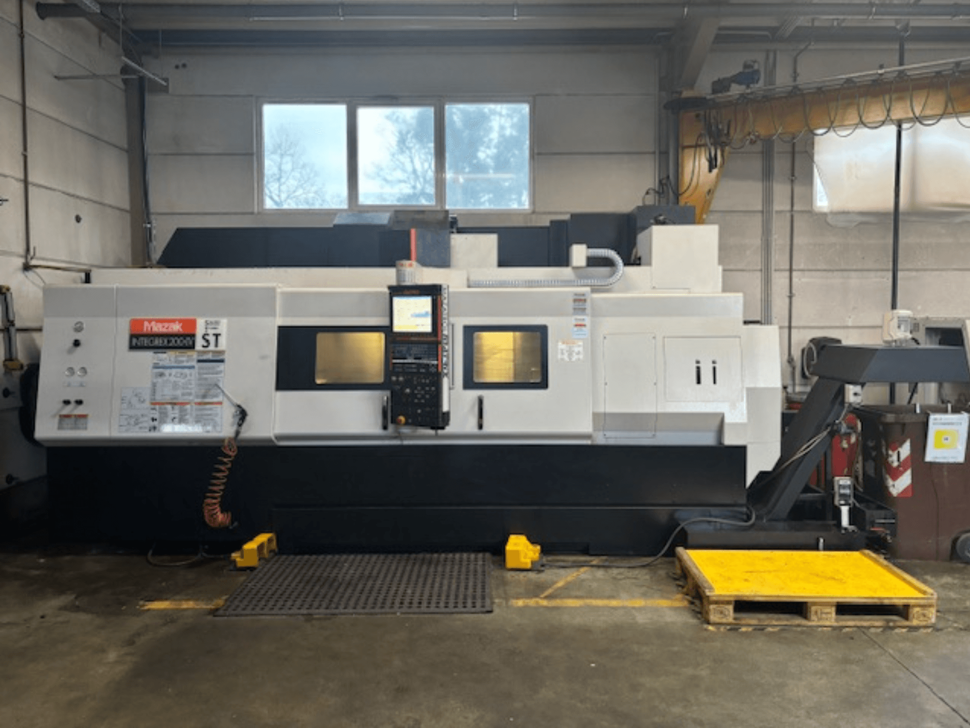 Mazak Integrex 200 SY ST, вид збоку, з панеллю керування, робочими дисплеями та лініями подачі охолоджувальної рідини в умовах майстерні.