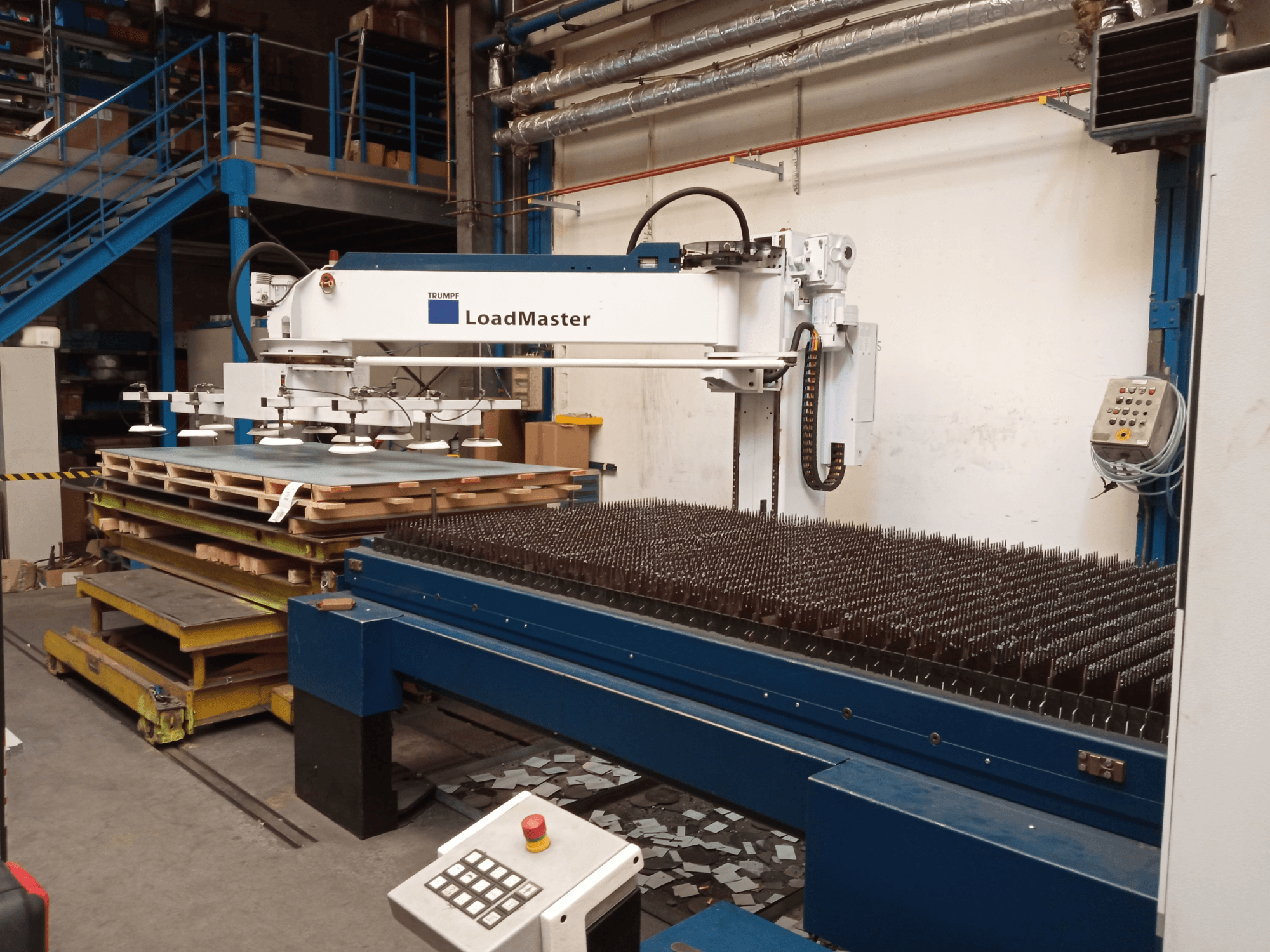 Лазерний верстат для різання CO2 TRUMPF TruLaser 3030 у боковому ракурсі, з системою LoadMaster та піддонами з матеріалами.