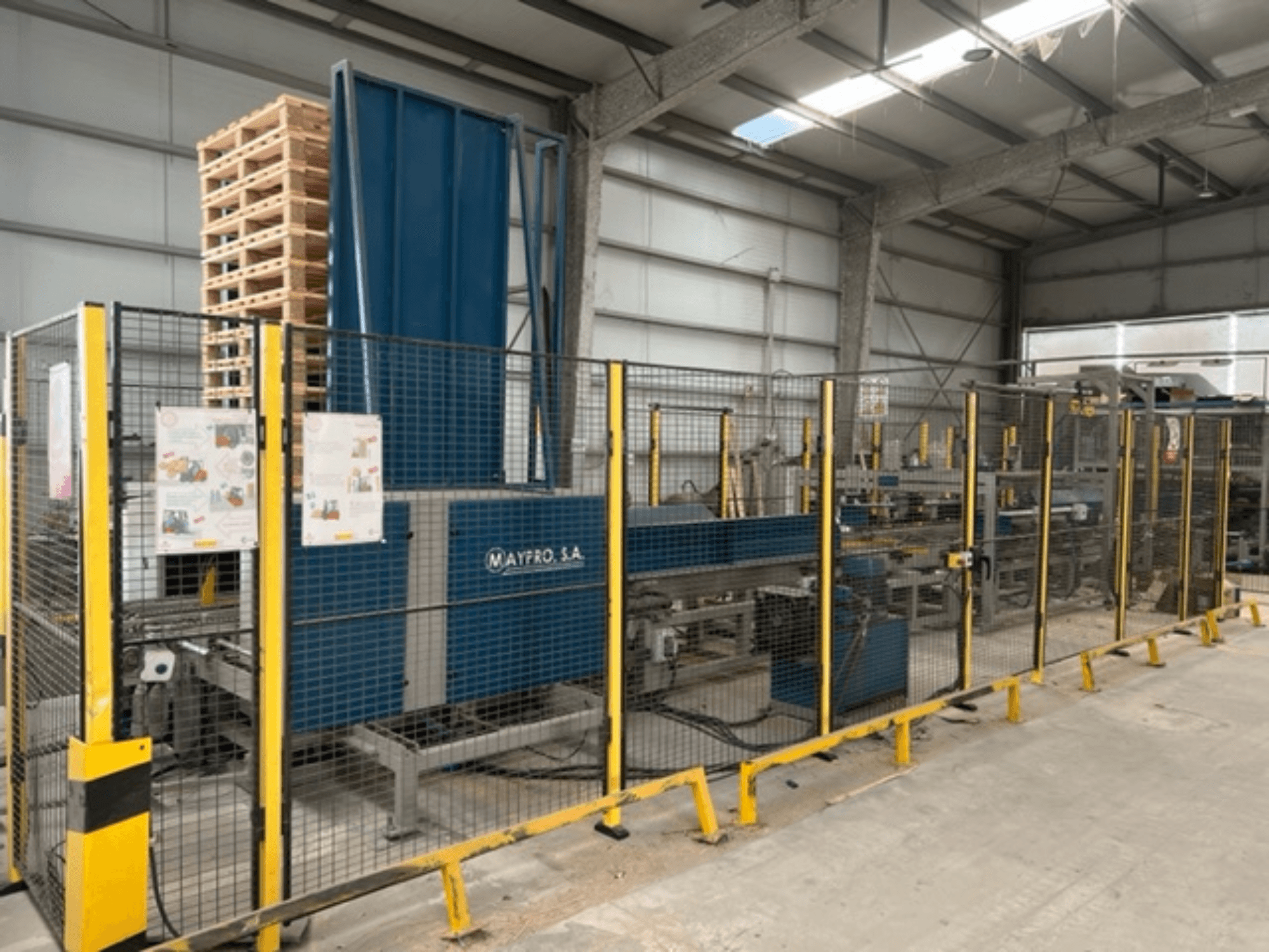 Промисловий пакувальник палет Maypro S.A. на складі, з захисною сіткою та органами керування, вид збоку.