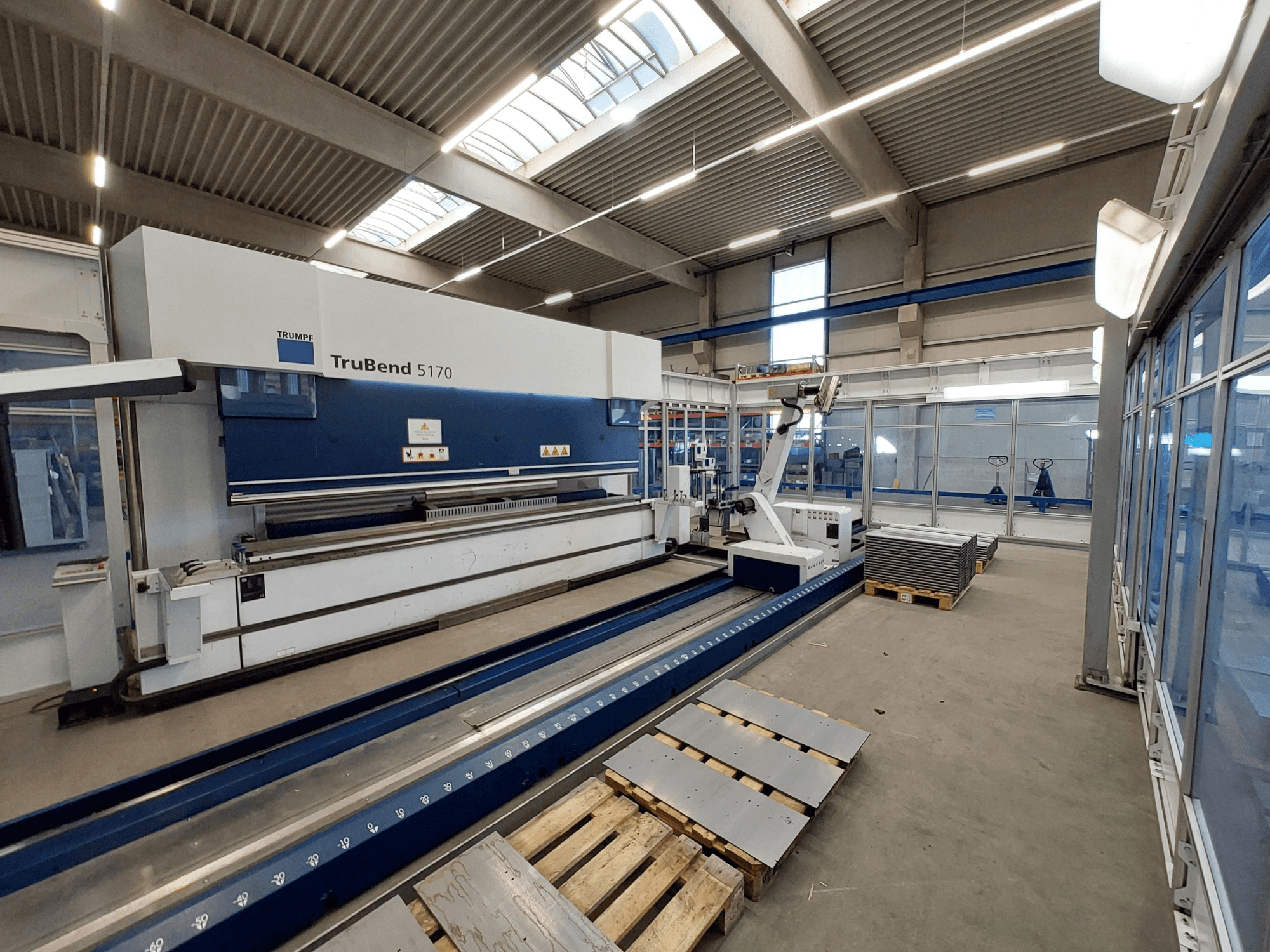 Листозгинальний прес TRUMPF TruBend 5170 у майстерні, вид збоку, показано інструмент для згинання та укладені на піддони металеві листи.