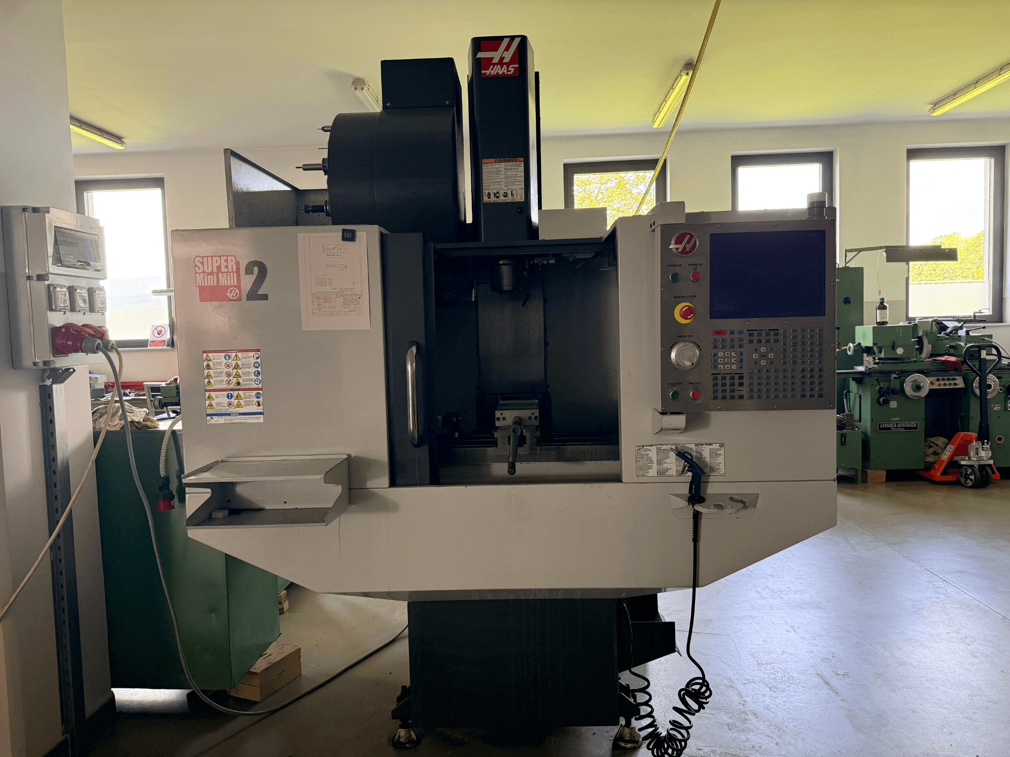 Вертикальний обробний центр Haas Mini Mill 2 у вигляді спереду, демонструючи панель керування та зону інструменту з попереджувальними написами.