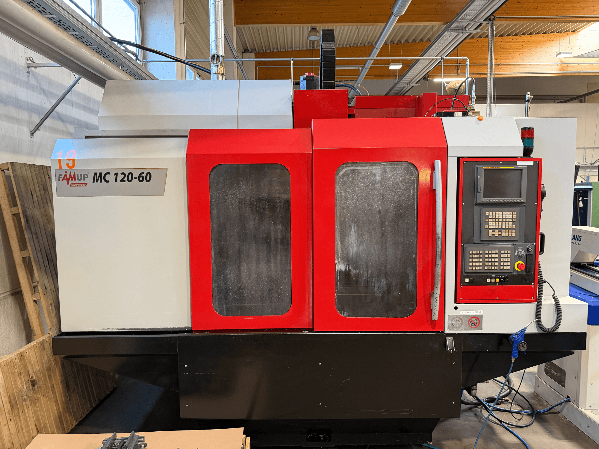 Вид спереду вертикального обробного центру EMCO MC 120-60 з червоно-білим корпусом, панеллю керування та екраном дисплея.