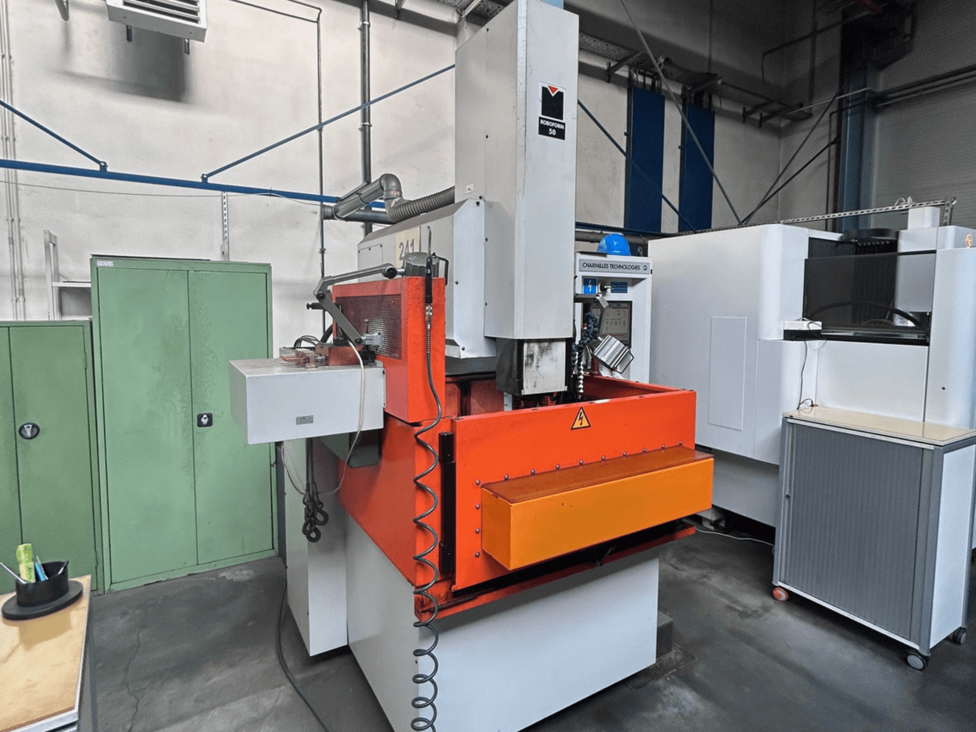 Вид спереду електроерозійного прошивного верстата CHARMILLES ROBOFORM 50 з помаранчевою панеллю, інтерфейсом керування та навколишнім обладнанням.