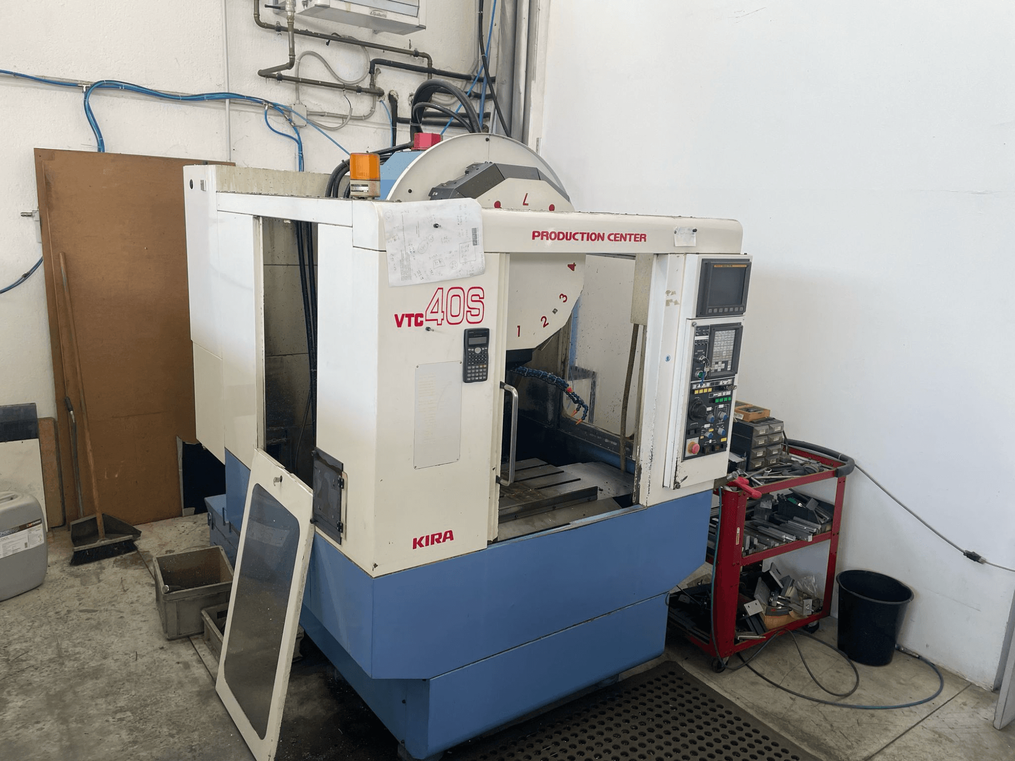 Обробний центр KIRA VTC 40S у вигляді збоку, з панеллю керування, відкритими дверцятами та інструментами на візку для зберігання поруч.