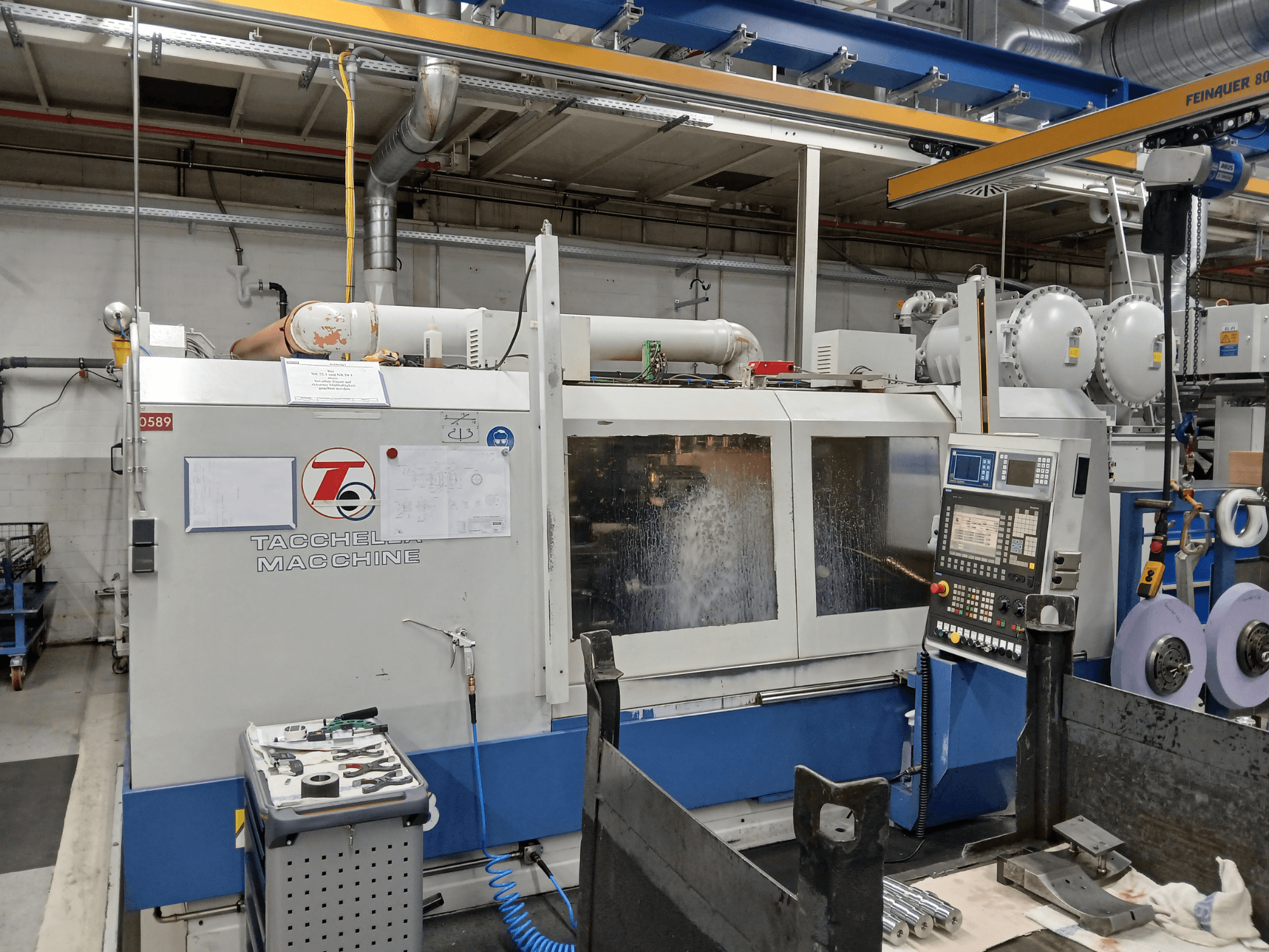 Обробний центр Tacchella спереду, видно панель керування та інструменти. Під час роботи розбризкується водяна охолоджуюча рідина.