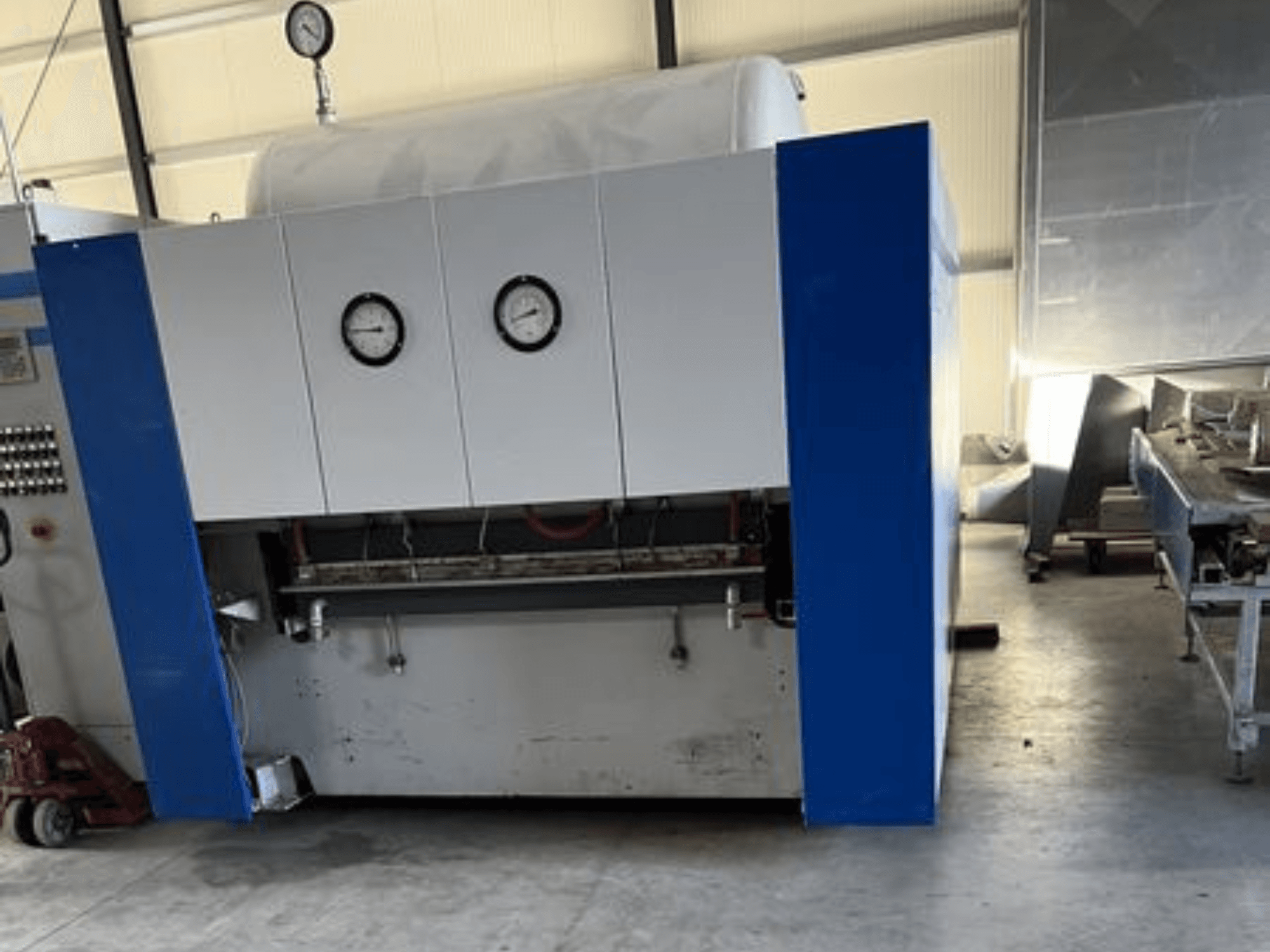 Синьо-біла промислова машина з двома манометрами, вид спереду, з панеллю керування та суміжним обладнанням.
