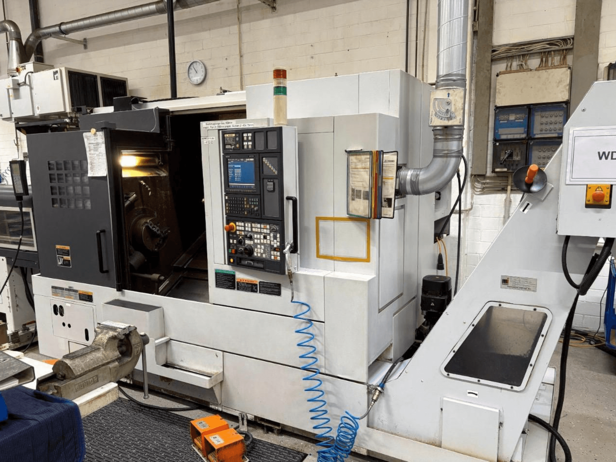 Токарно-фрезерний центр MORI SEIKI NL 2500 SY, вид спереду, з панеллю керування та зоною обробки. Видима система охолодження та аксесуари.