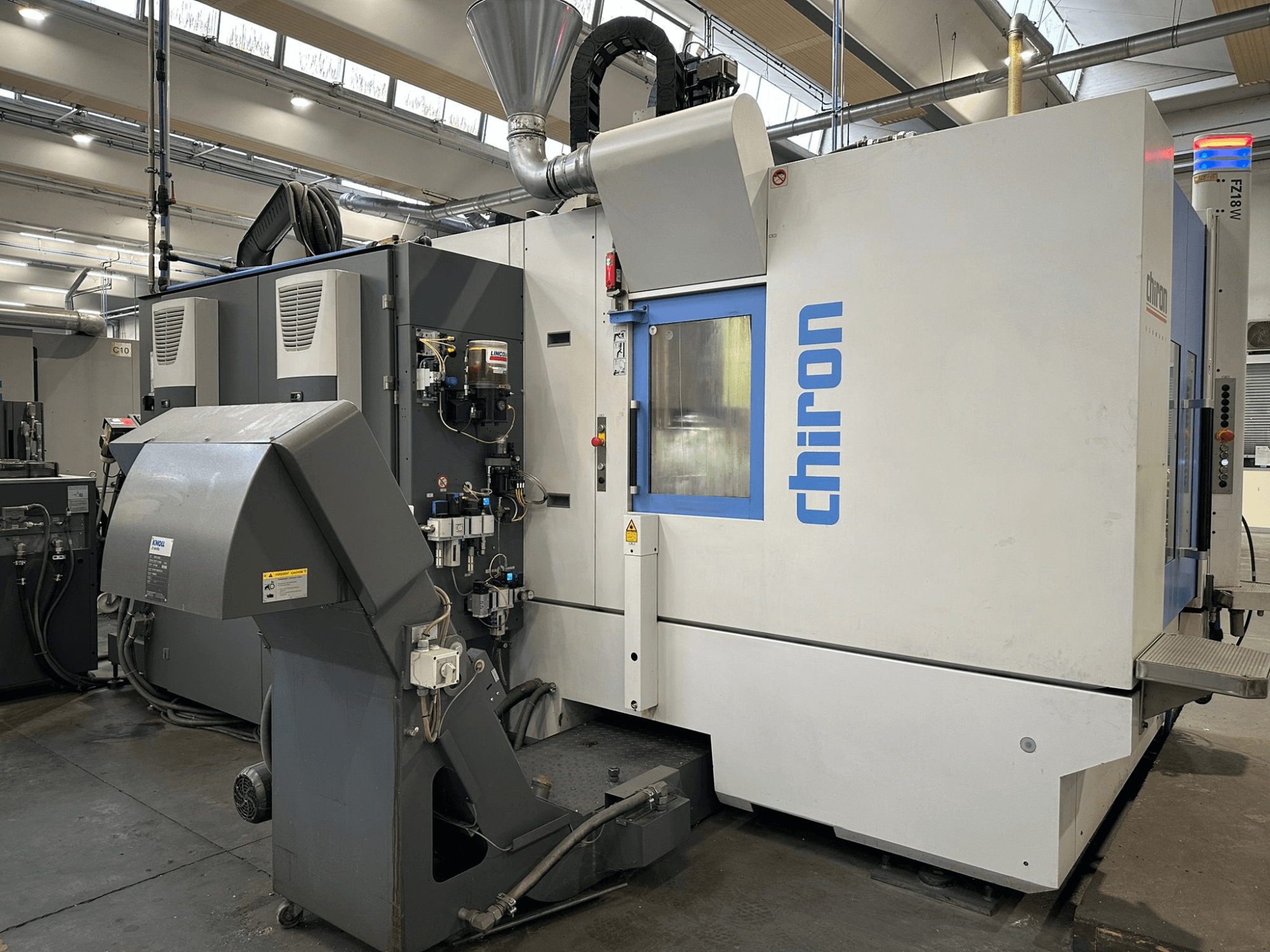 Верстат з ЧПК Chiron у сіро-білому кольорі, вид спереду, з елементами керування, трубами та витяжкою для відсмоктування пилу.