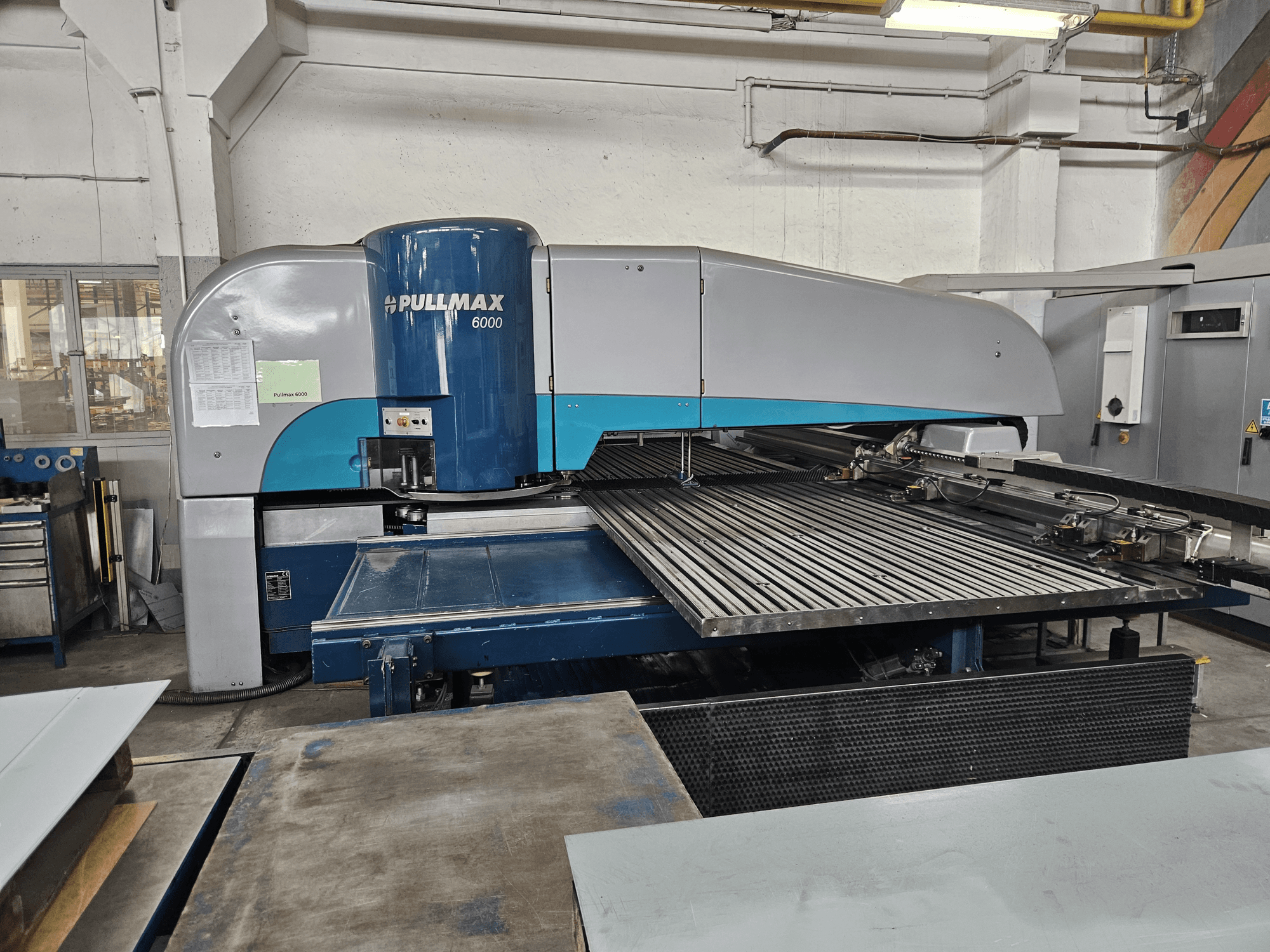 Вид спереду на штампувальний верстат з ЧПУ Pullmax 6000, що демонструє його велику платформу і металеву раму в умовах майстерні.