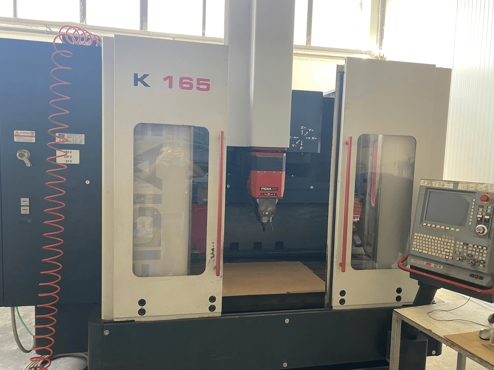 Верстат з ЧПК Fidia K 165 з червоним шпинделем і панеллю керування, вид спереду, в добре освітленому цеху.