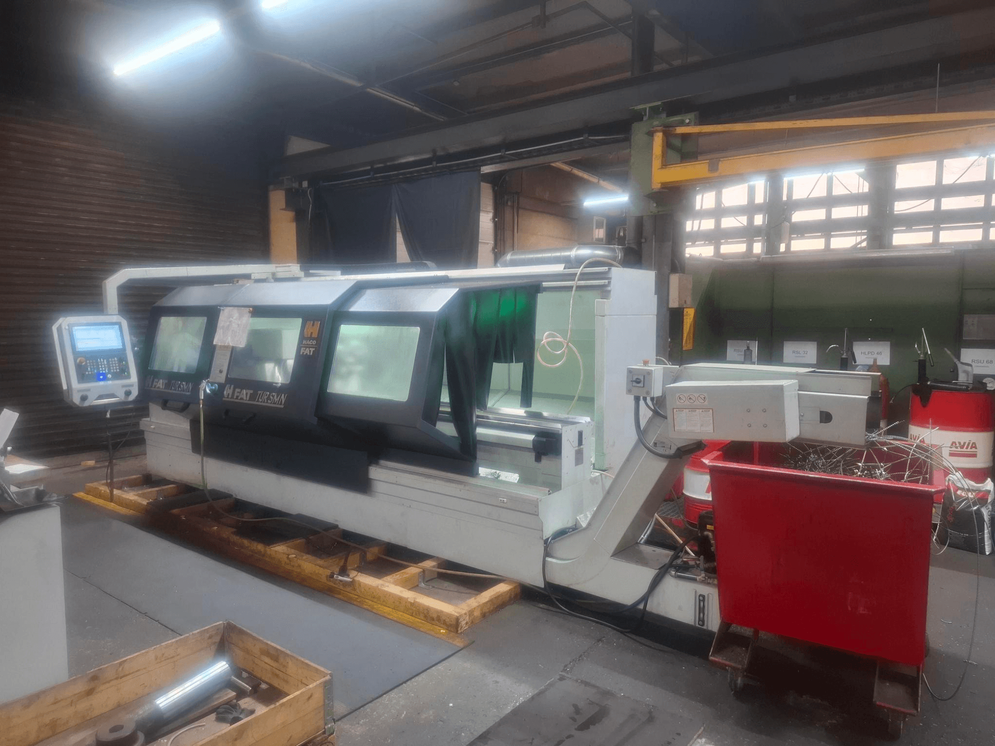 Вид спереду верстата з ЧПК FAT Tursan з панеллю керування, розміщеного на дерев'яних піддонах у майстерні.
