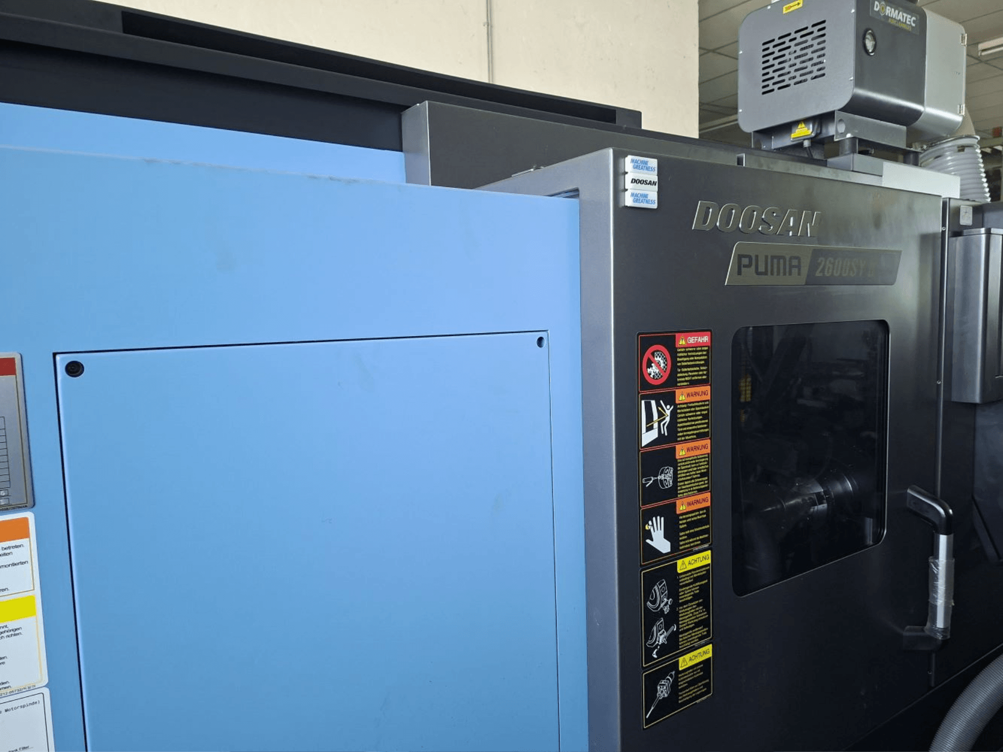 Горизонтальний токарний верстат DOOSAN PUMA 2600 SY II, вид спереду, з етикетками безпеки та синьою панеллю.