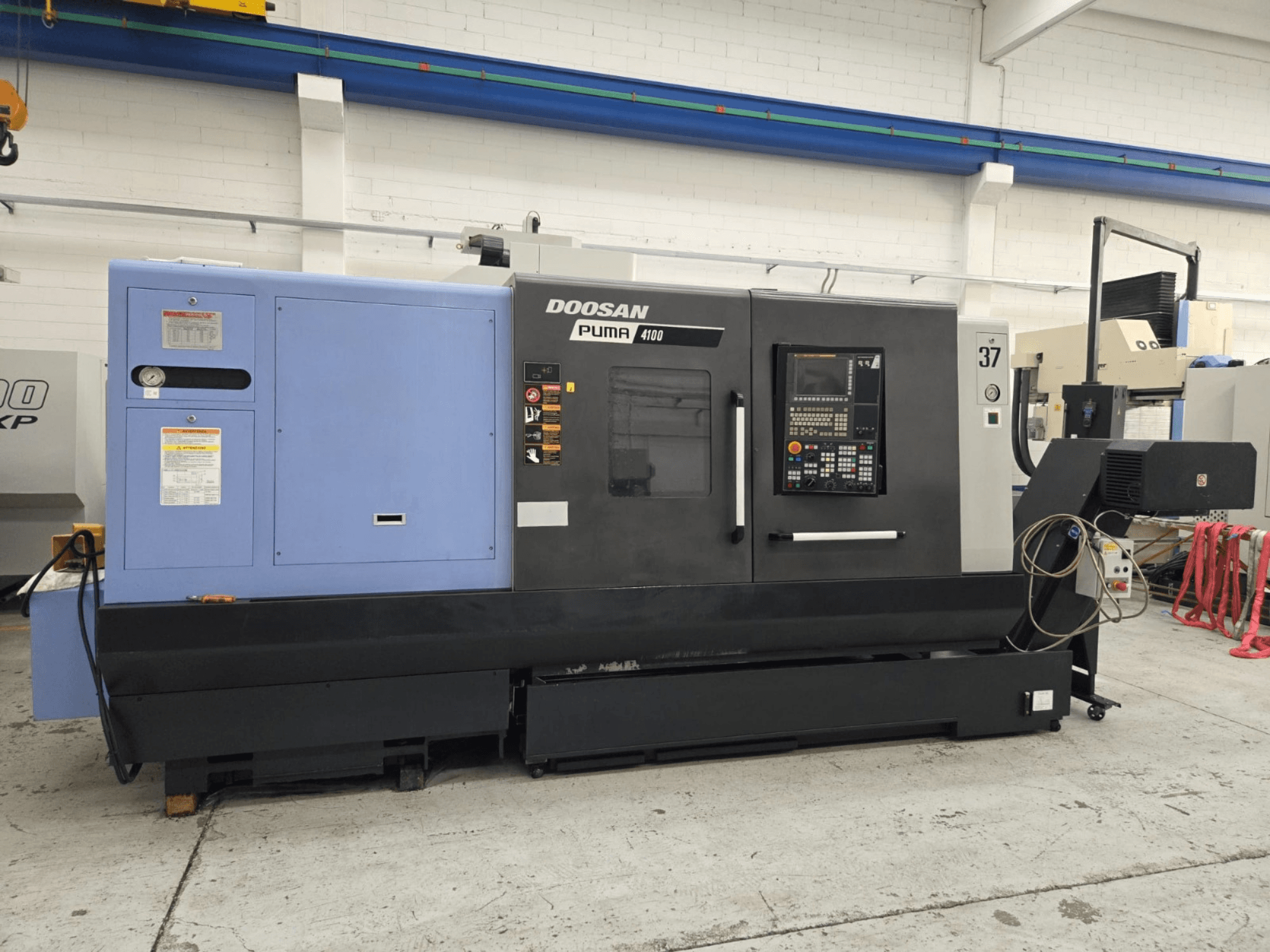 Токарний верстат з ЧПК Doosan Puma 4100, вигляд спереду; панель керування, синій блок живлення та детальні етикетки для інструкцій з експлуатації.