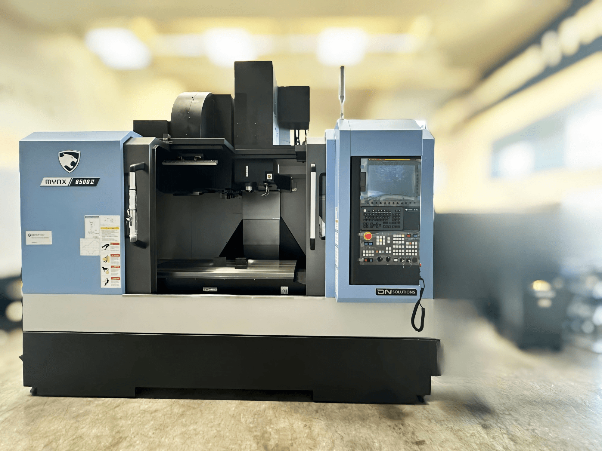 Вертикальний обробний центр DN SOLUTIONS MYNX 6500 II, вид спереду, на якому видно панель управління та робочу зону.