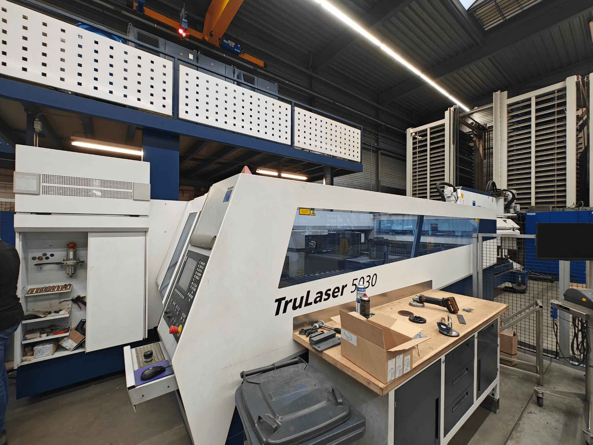 Верстат TruLaser 5030 в майстерні, вид спереду з видимою панеллю керування, в оточенні інструментів та обладнання.