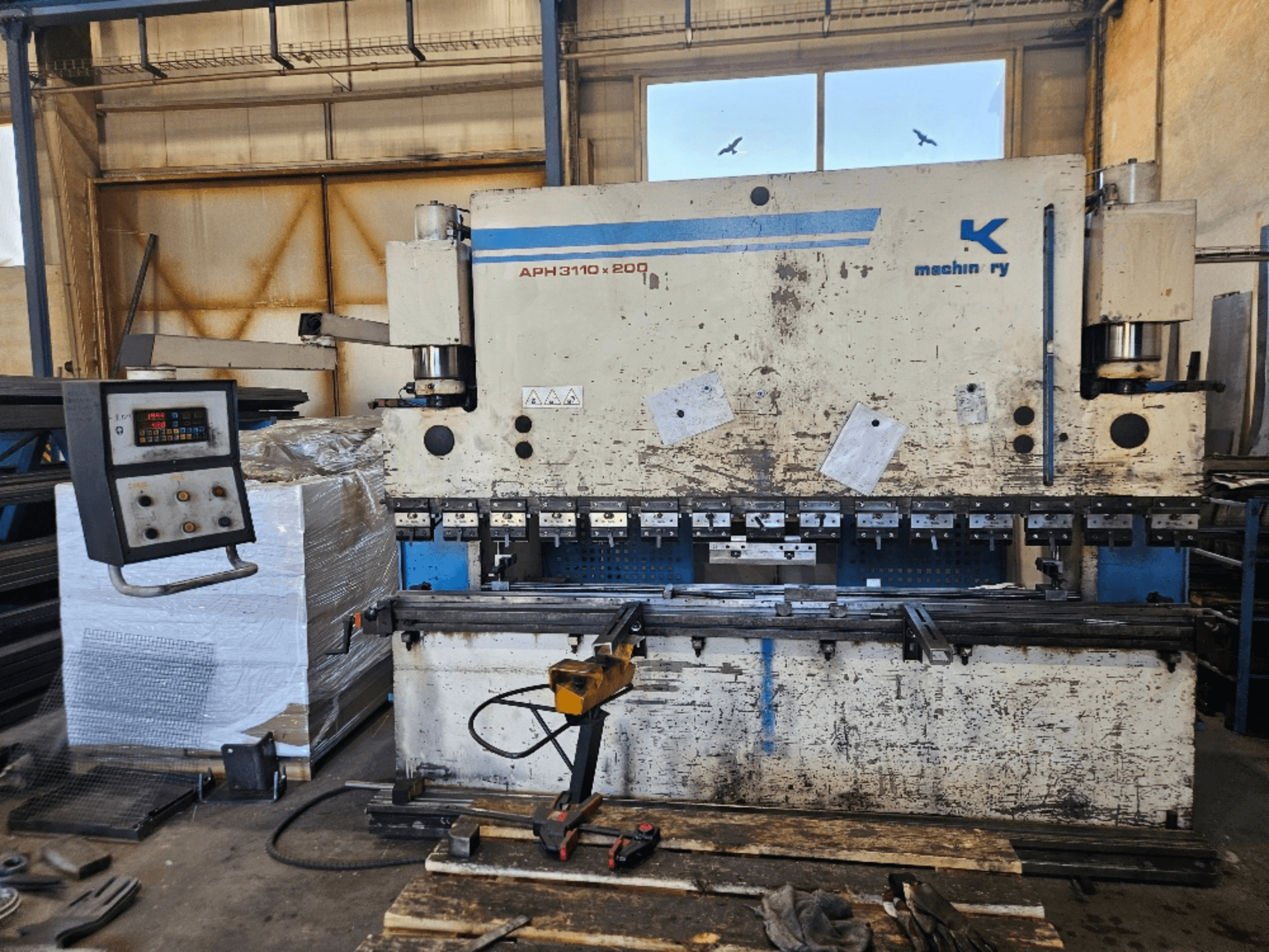 Пресовий гальмо Baykal APH 3110x200 в майстерні, вид спереду, з панеллю керування, металевими листами та інструментами.