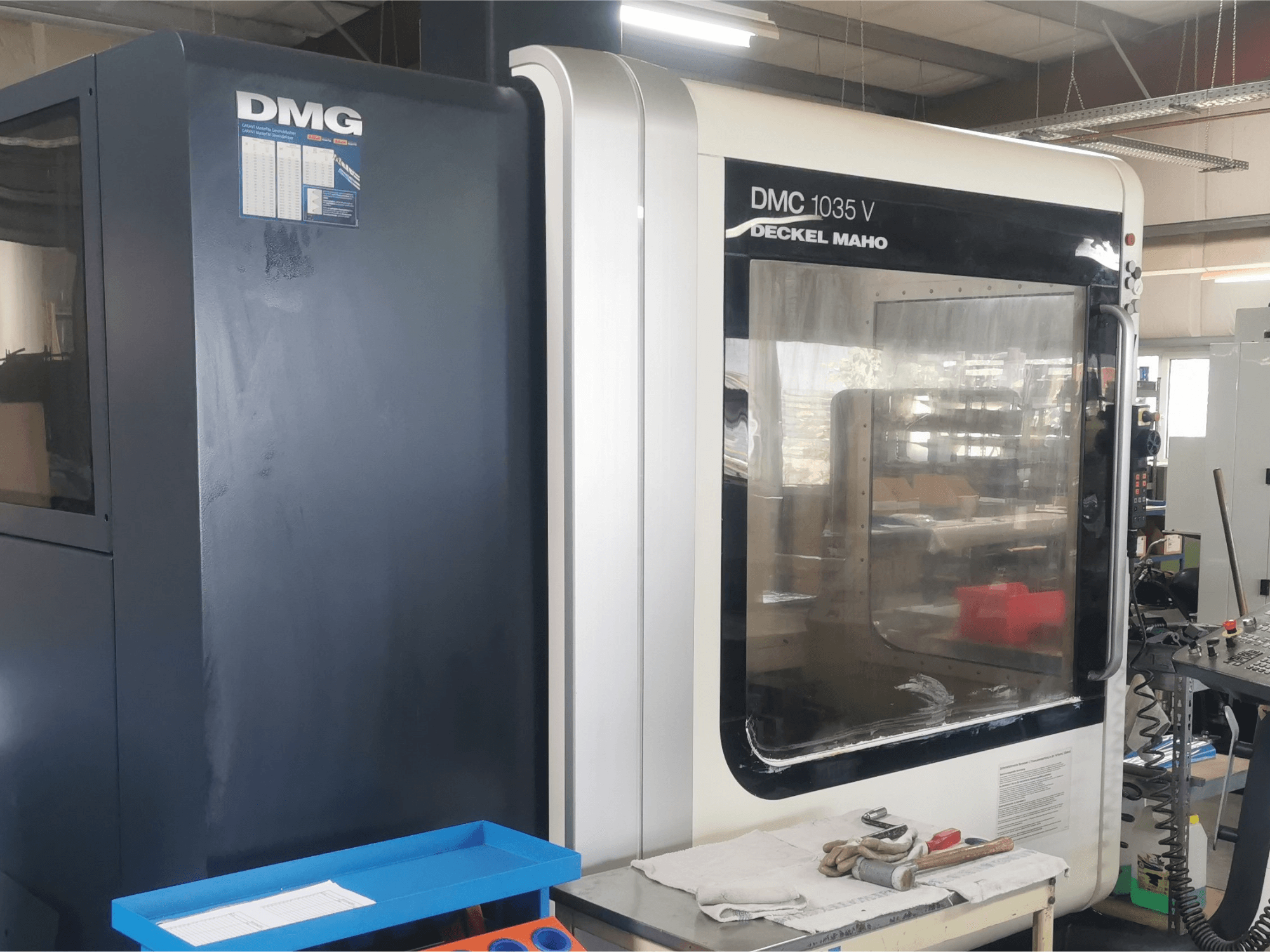 Фрезерний верстат DMG DMC 1035 V в майстерні, вид спереду з синім лотком для інструментів і рукавичками на поверхні.