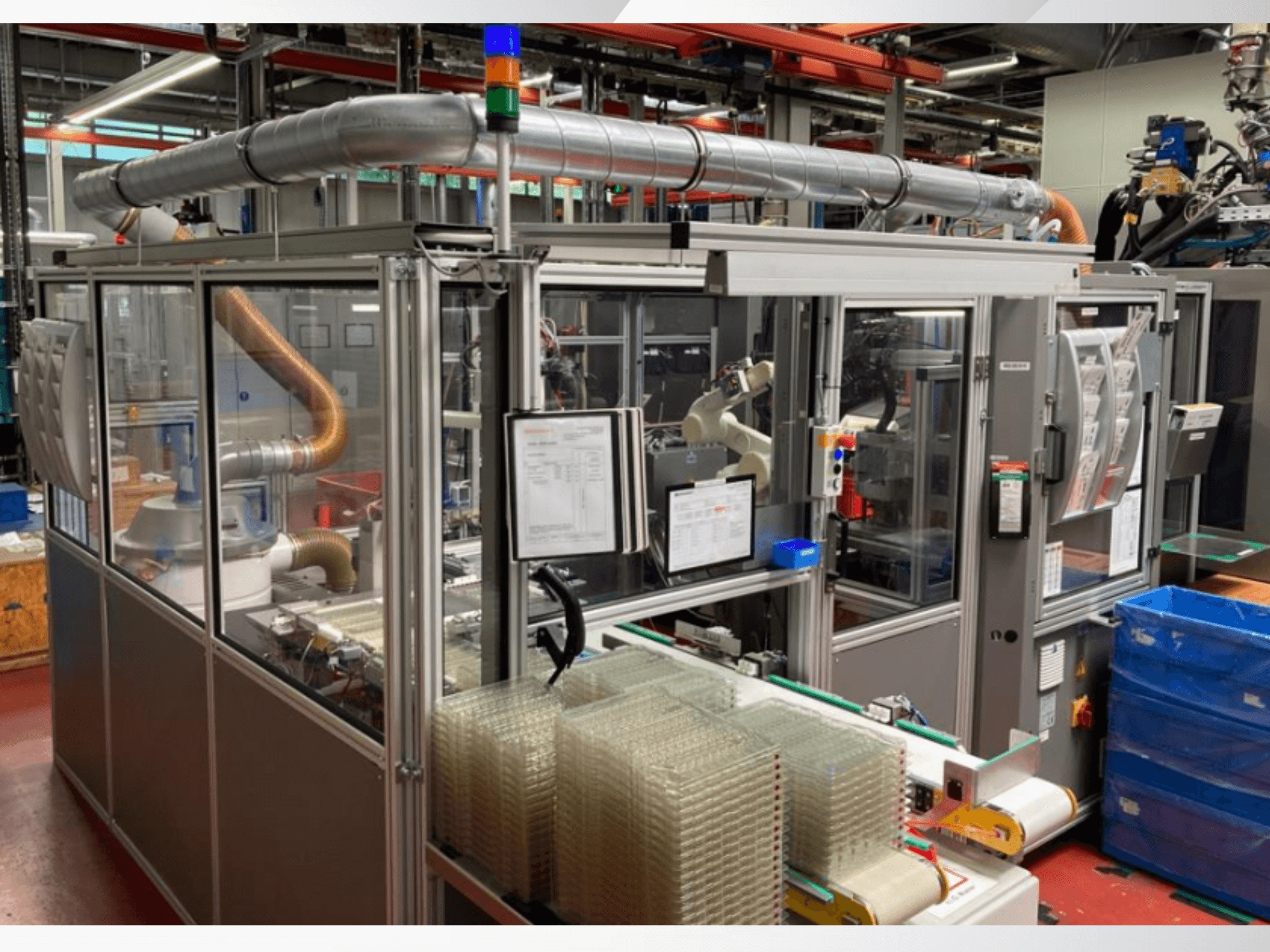 Автоматизована складальна машина з роботизованою рукою, прозорими бічними панелями та штабелями прозорих контейнерів, вид спереду.
