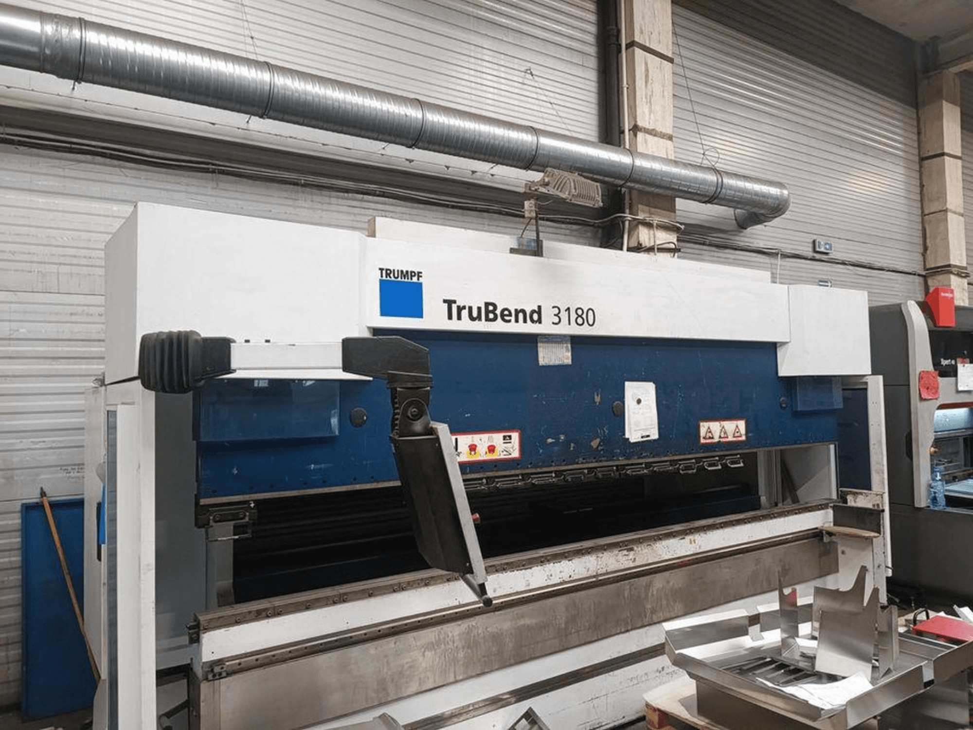 Згинальний верстат Trumpf TruBend 3180 в майстерні, вид збоку: панель керування та металеві деталі на столі.