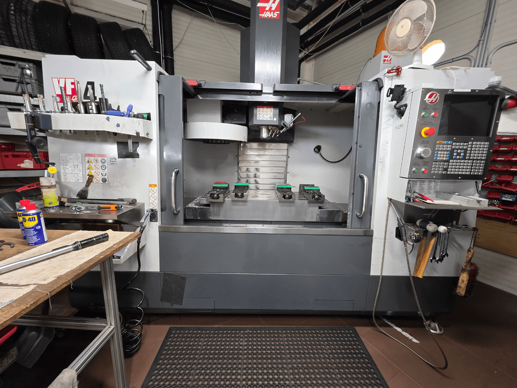 Фрезерний верстат Haas VF-4 з ЧПК спереду в майстерні, з інструментами, комп'ютерним інтерфейсом і двома заготовками на столі.