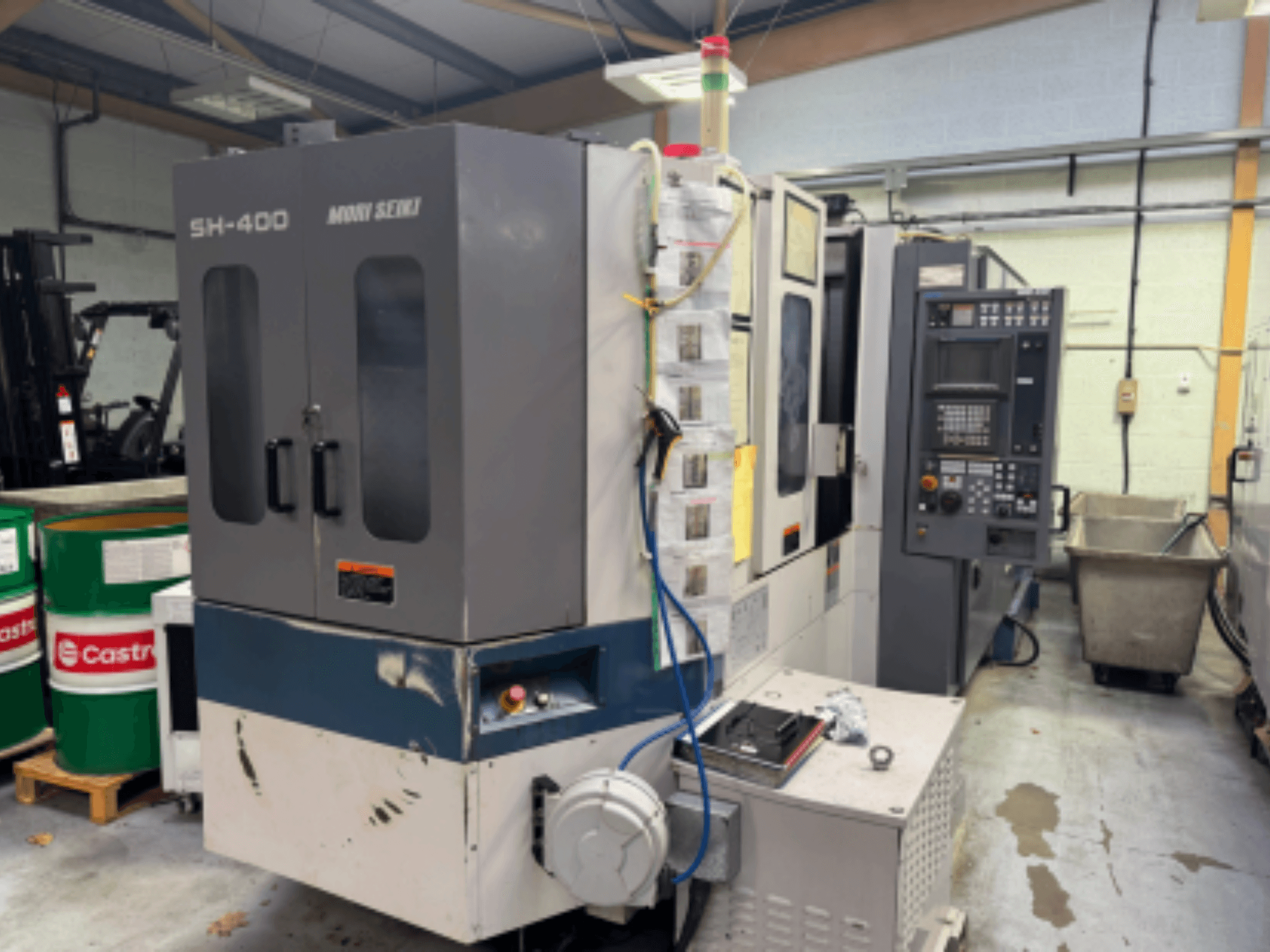 Верстат з ЧПК Moni Seiki SH-400, вид збоку: панель керування, двері та навколишнє промислове середовище.
