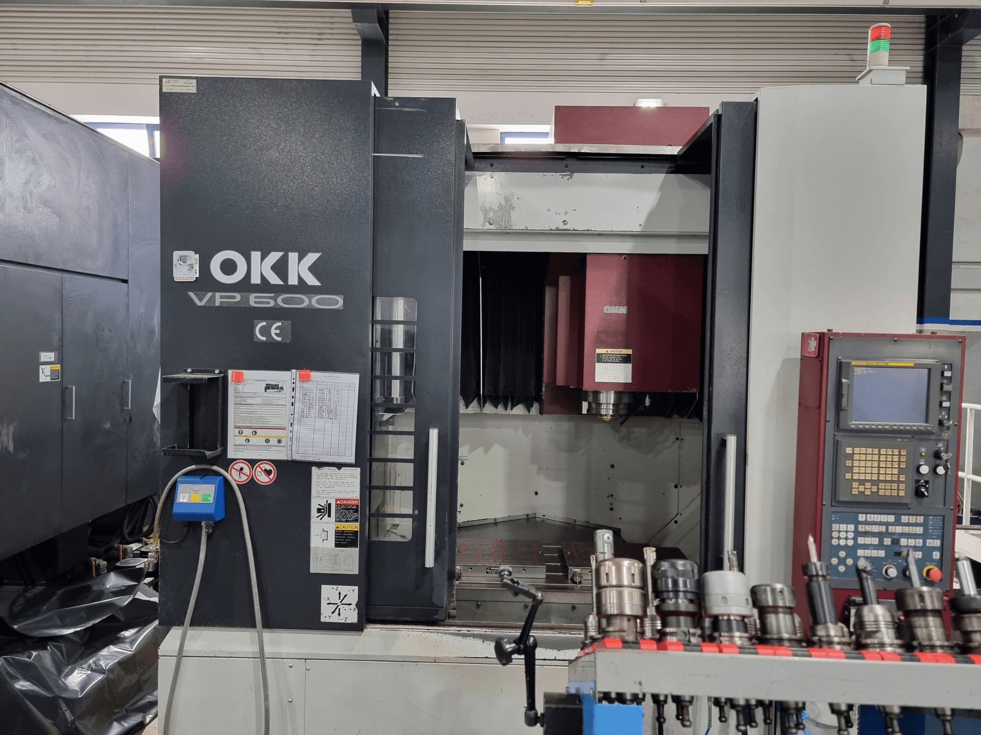 Вертикальний обробний центр OKK VP600 у фронтальному ракурсі: на фото видно панель управління та тримачі інструментів на стійці.