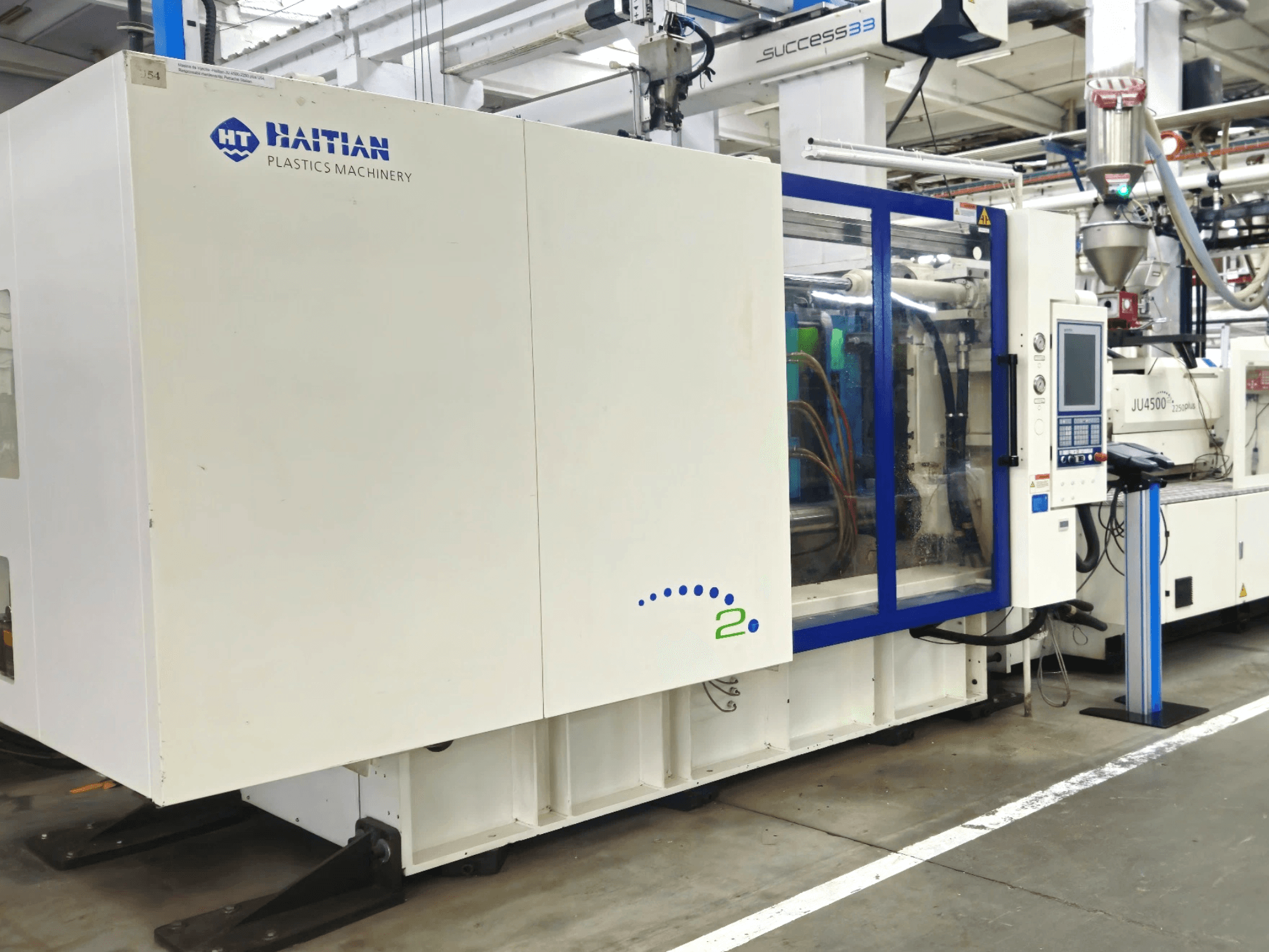 Модель Haitian Plastics Machinery, вид спереду, демонструє обладнання з панеллю керування та видимими трубами в промислових умовах.