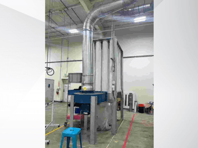 Велика промислова вентиляційна система, вид спереду, з блискучими металевими повітроводами та синьою основою, розташована на просторому складі.