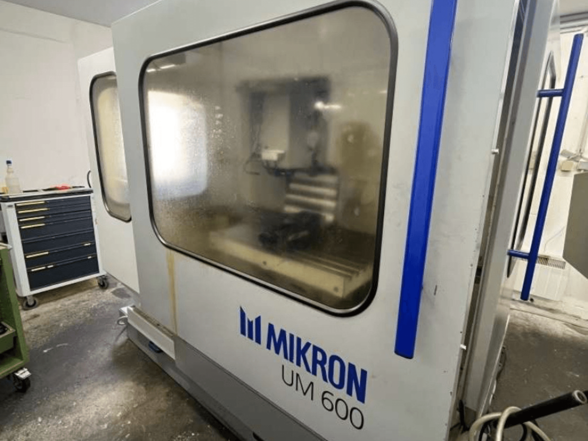 Універсальний обробний центр MIKRON UM 600 TNC 410/426, вид збоку, з запітнілим склом і видимим місцем для зберігання інструменту.