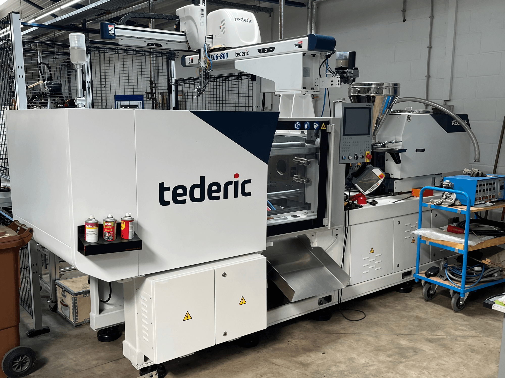 Гідравлічна машина для лиття під тиском TEDERIC NEO.E55/e110h у цеху, вид збоку з панеллю управління та сусіднім інструментом.