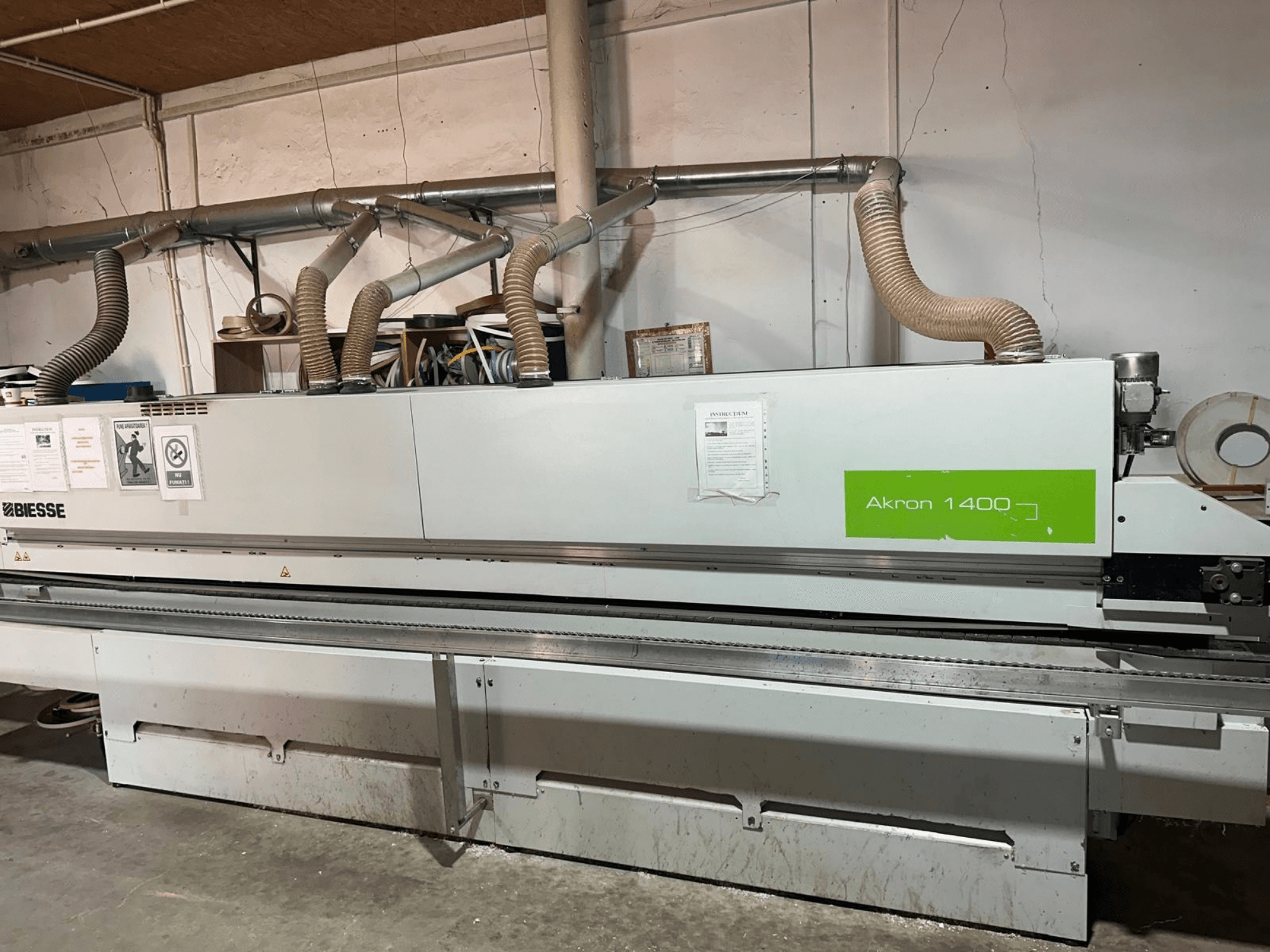 Кромкооблицювальна машина BIESSE Akron 1440 A у боковому ракурсі, з витяжною системою, панеллю керування та наклейками з інструкціями щодо експлуатації.