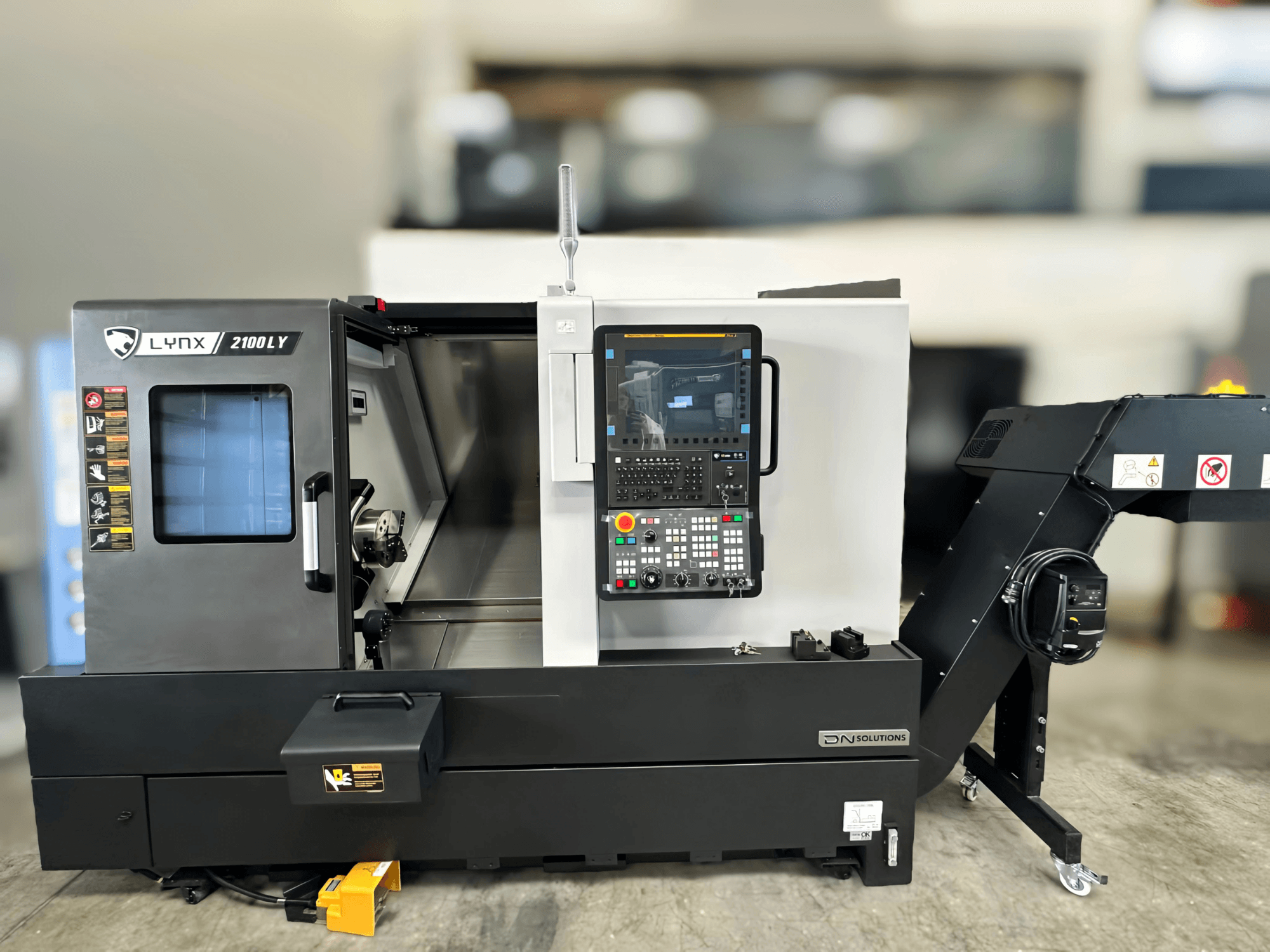 Горизонтальний токарний верстат DN SOLUTIONS LYNX 2100LYB, вид спереду, з панеллю керування і відкритими дверцятами, що відкривають внутрішній простір.