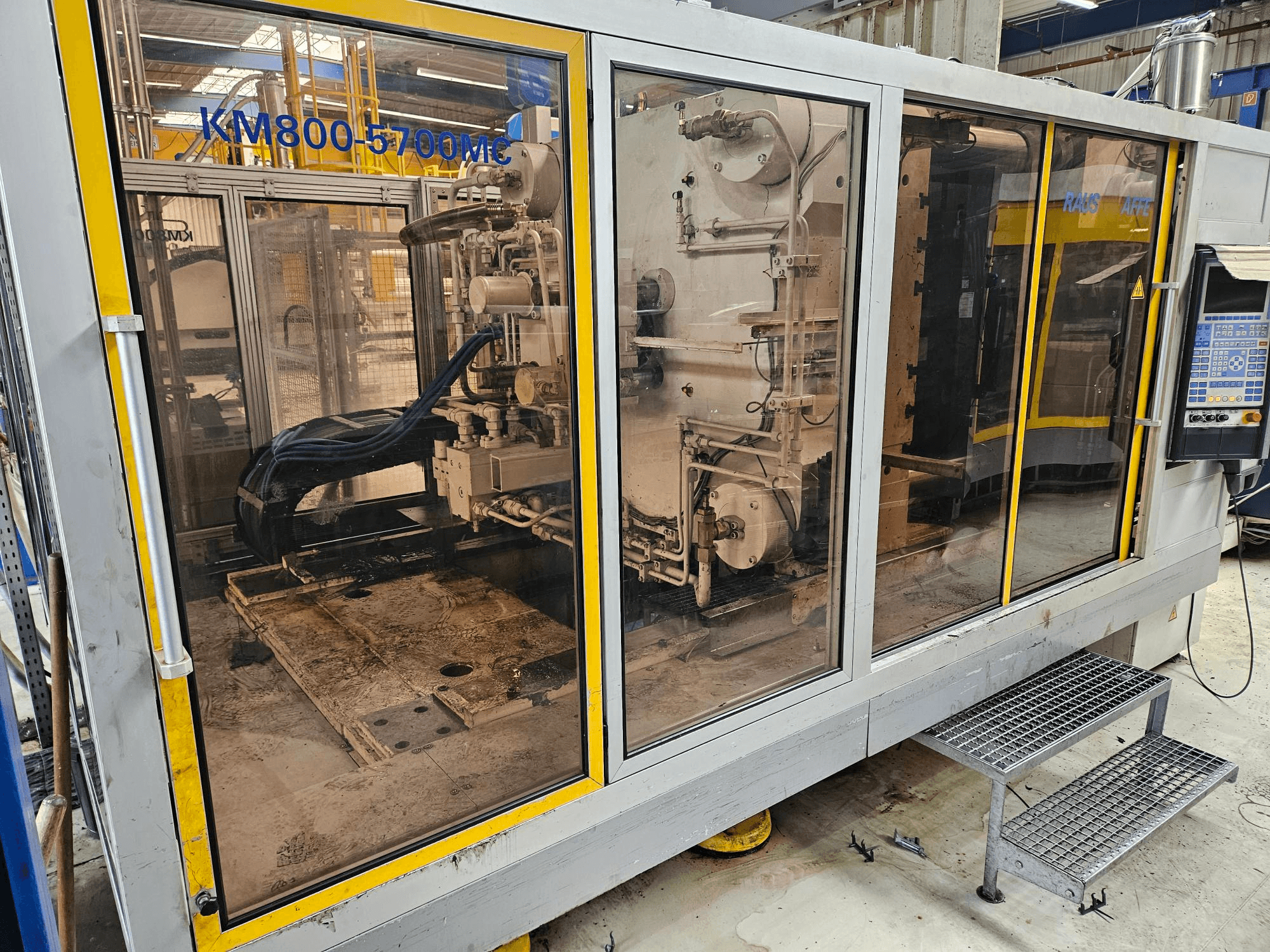 Гідравлічна термопластавтомат Krauss Maffei KM800-5700 MC, вид спереду, що демонструє компоненти крізь скляні панелі.