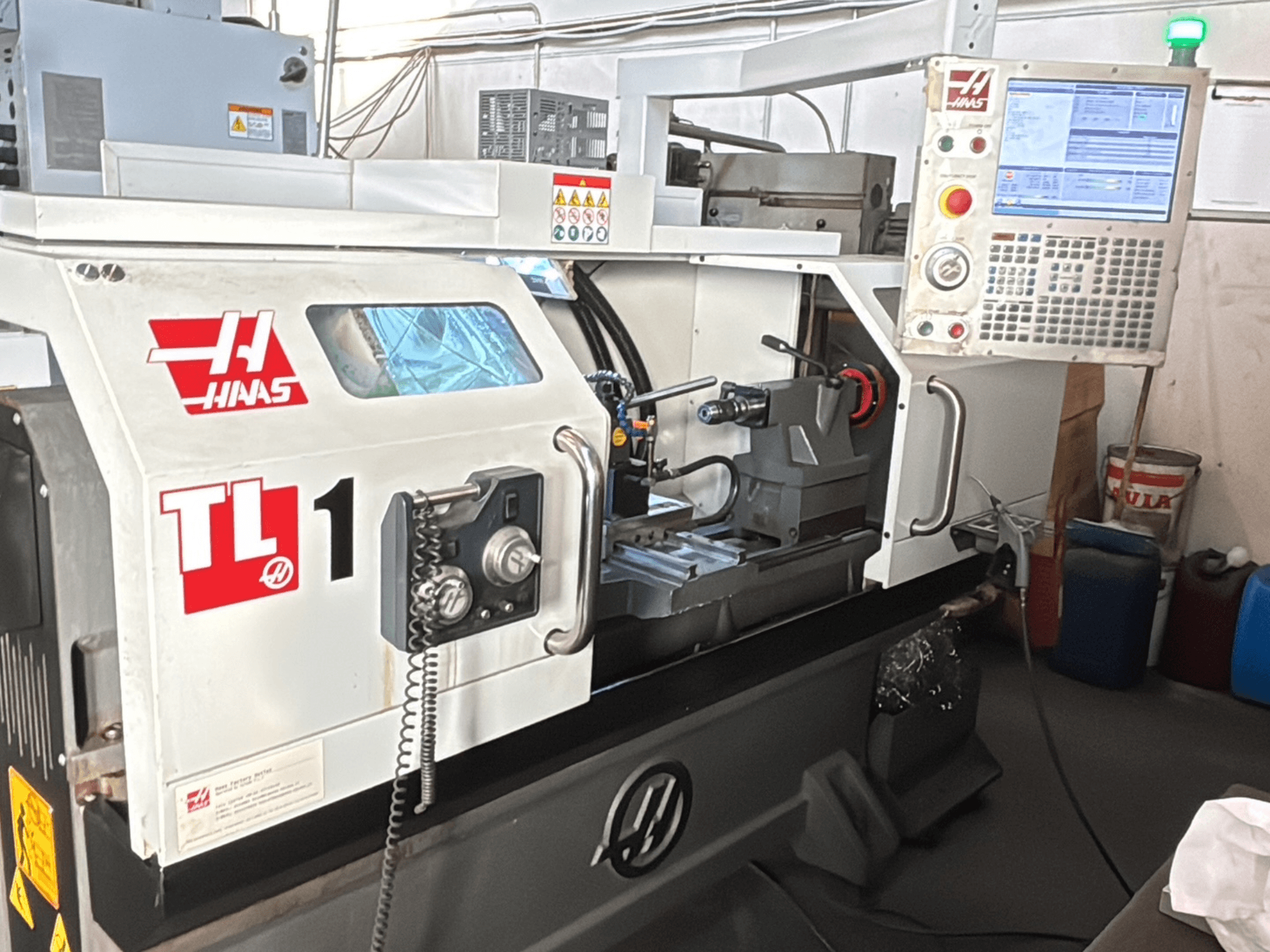 Токарний верстат з ЧПК Haas TL-1, вид спереду, оснащений панеллю керування з дисплеєм, тримачем інструменту та етикетками безпеки.
