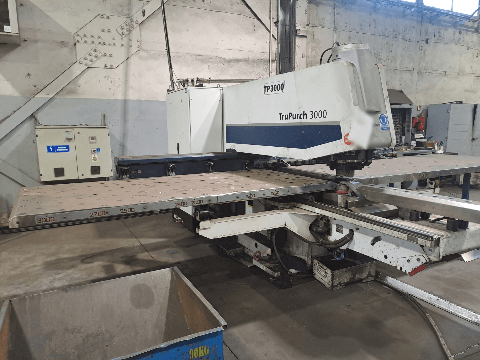 Верстат TruPunch 3000 з ЧПУ показаний спереду, з великою металевою пластиною і розміткою для вимірювання, в промислових умовах.