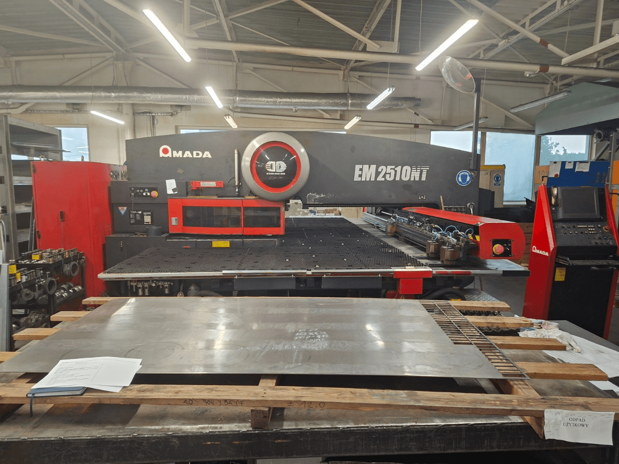 Вид спереду револьверного штампувального преса AMADA EM 2510NT з металевим листом і панеллю керування в умовах майстерні.