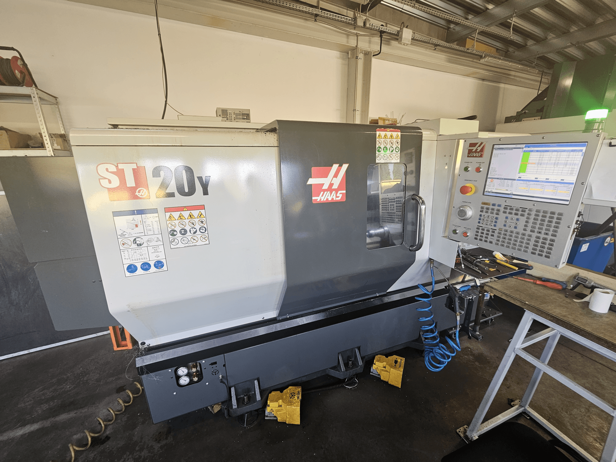 Токарний верстат з ЧПК Haas ST-20Y, вид спереду з панеллю керування; збоку - етикетки безпеки та деталь повітряного шланга.