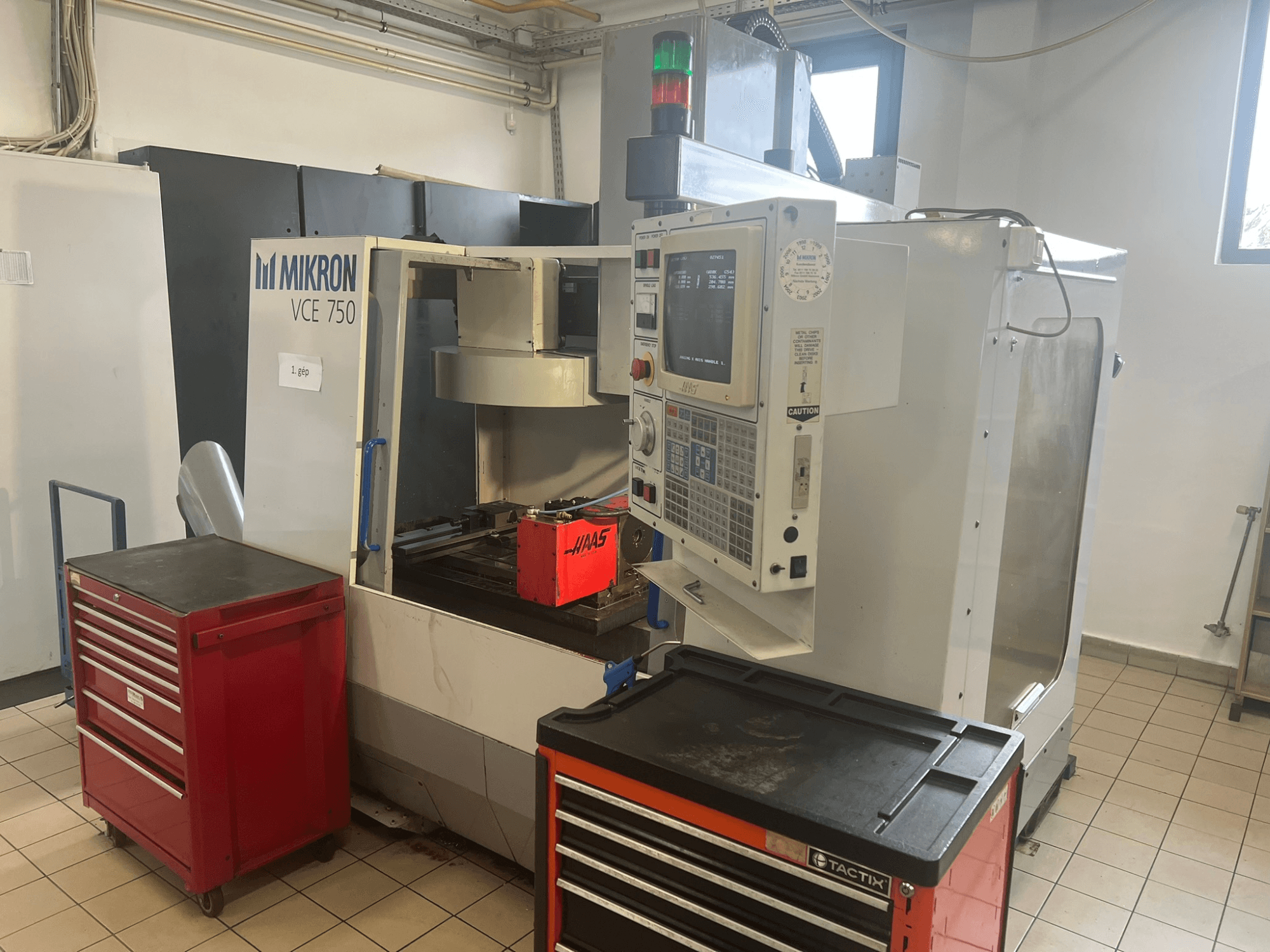 Інший текст: "Вертикальний обробний центр MIKRON VCE 750, вид спереду з панеллю керування та червоними ящиками для інструментів у просторому цеху".