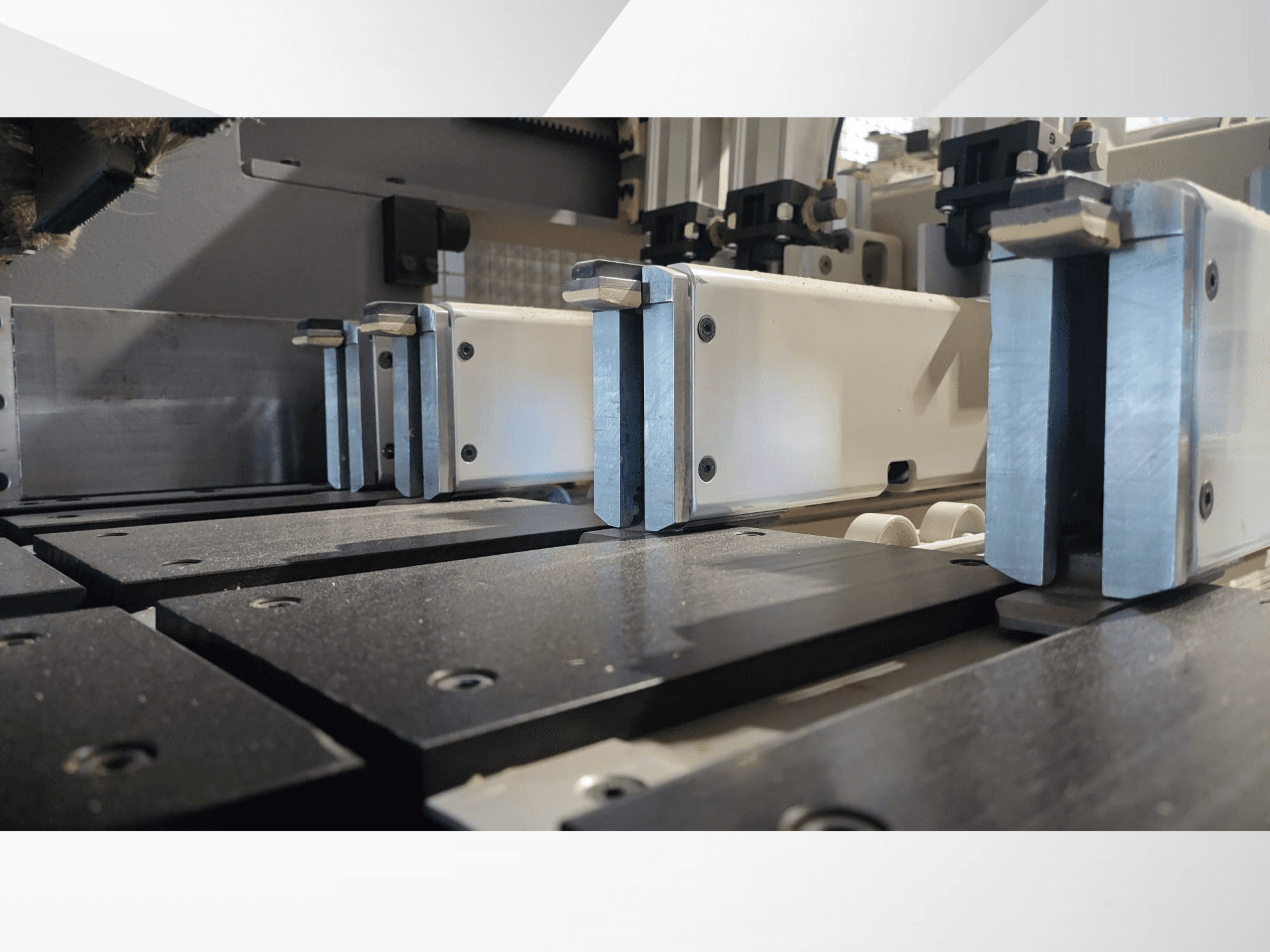 Крупний план затискного механізму прецизійного верстата з металевими губками, з чорними робочими поверхнями та видимими напрямними.