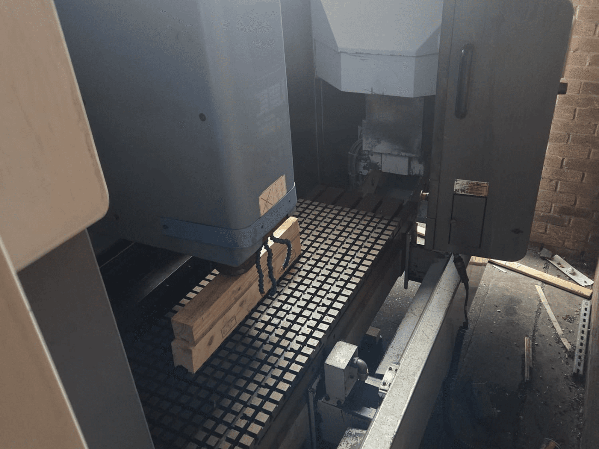 Вид спереду верстата з ЧПУ з дерев'яними дошками на сітчастому столі, збоку демонструються інструменти та елементи керування.