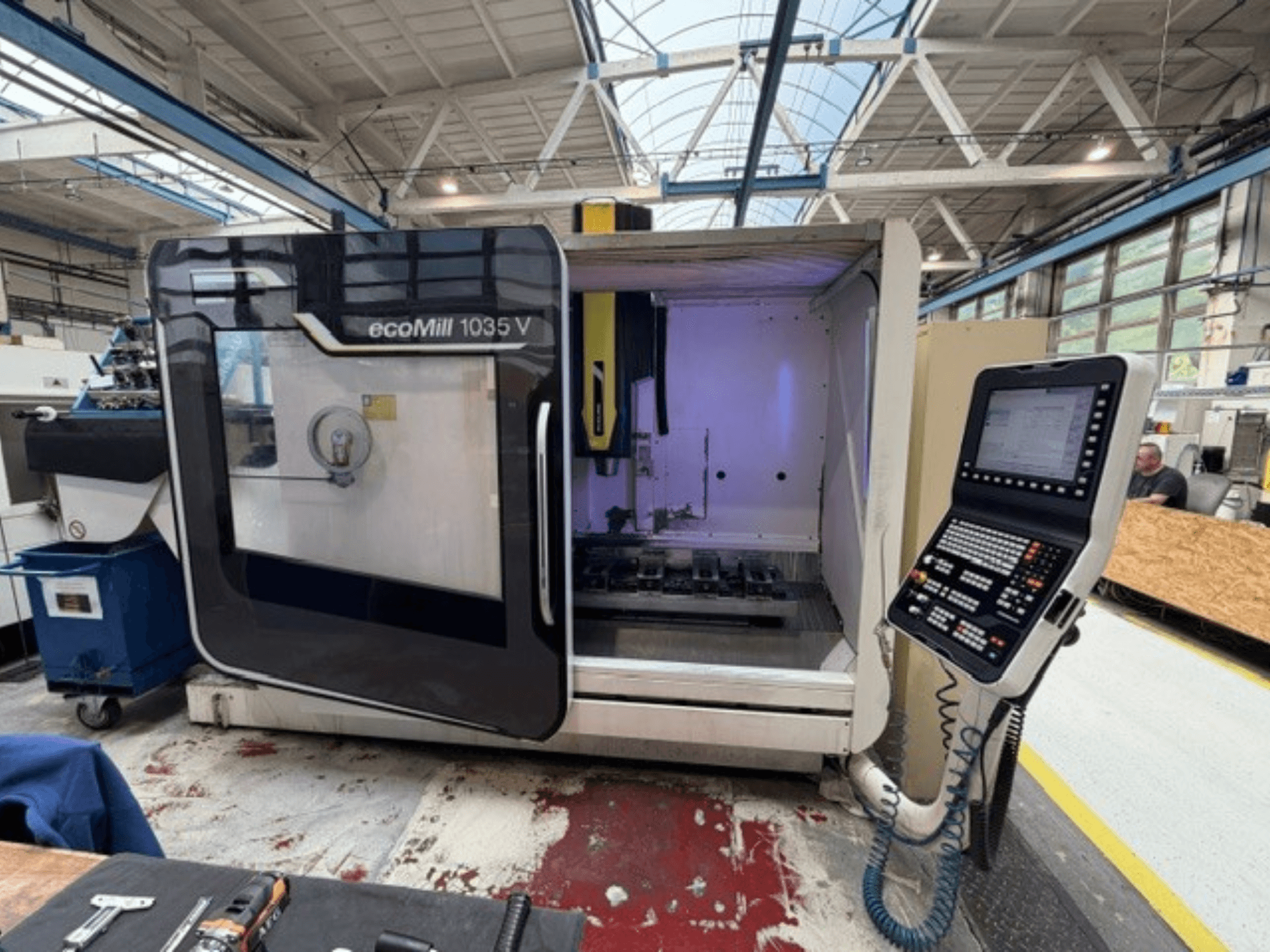 Вигляд спереду вертикального обробного центру DMG MORI ecoMill 1035V з відкритими дверцятами, на якому видно панель управління та робочу зону всередині.