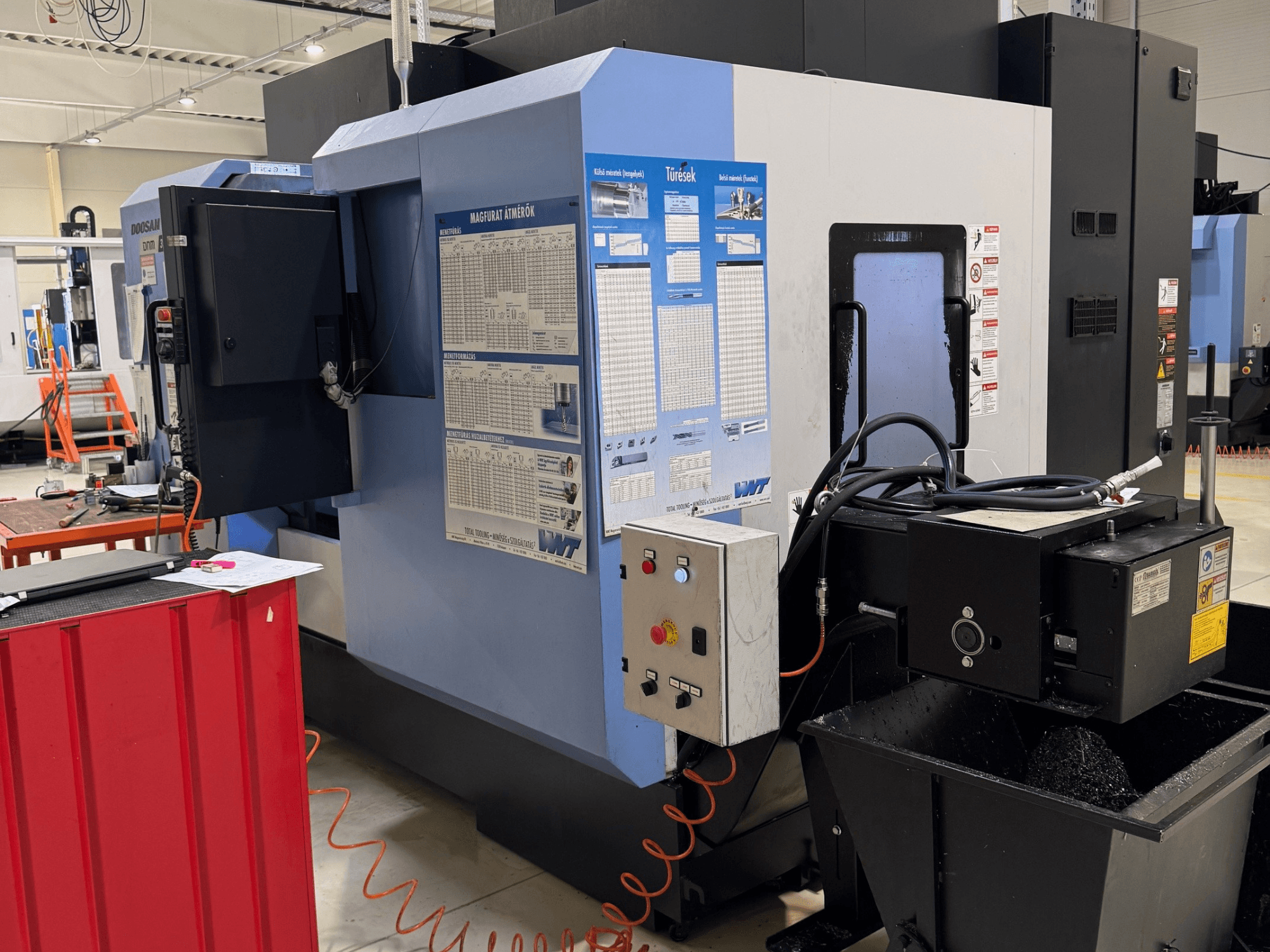 Токарно-фрезерний центр DOOSAN DNM350/5AX, вид збоку, на якому видно панель управління та бак для охолоджувальної рідини, а також деталі робочого процесу.