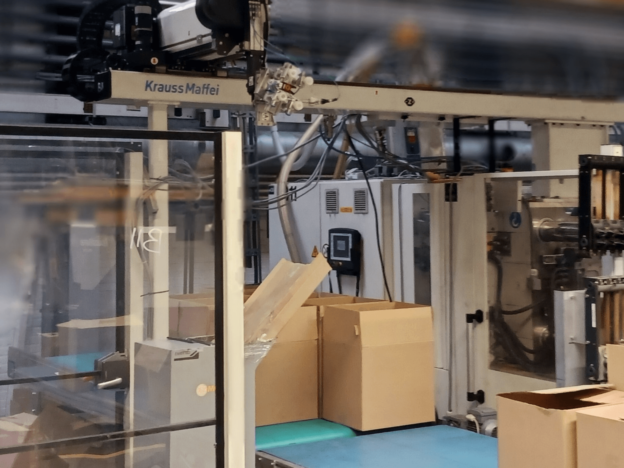 Система автоматизації Krauss Maffei на заводі, вид спереду: коробки на конвеєрі та компоненти машин в роботі.
