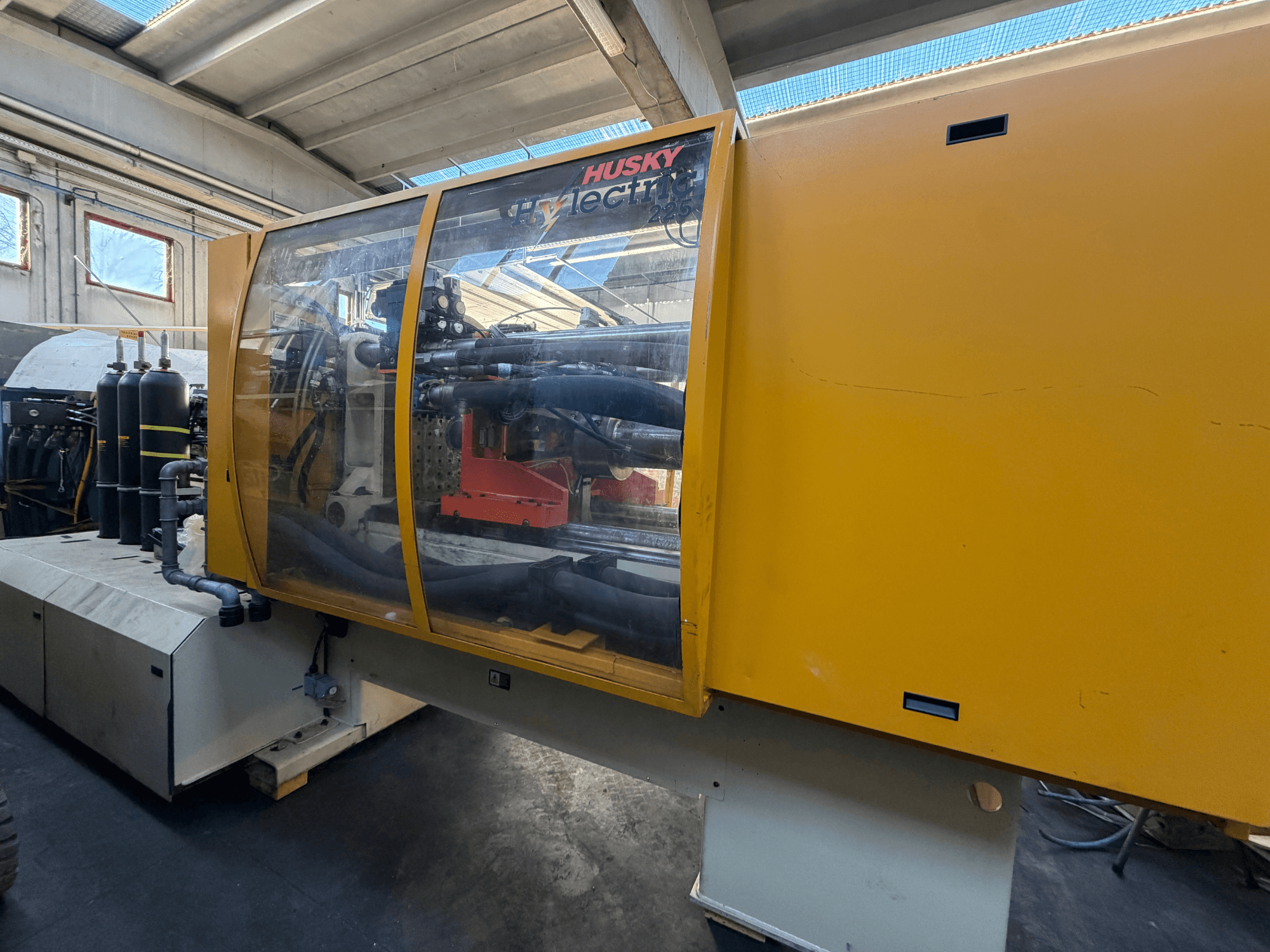 Електрична термопластавтомат Husky HL225 RS65, вид спереду з жовтим корпусом, видимою панеллю керування та гідравлічними компонентами.
